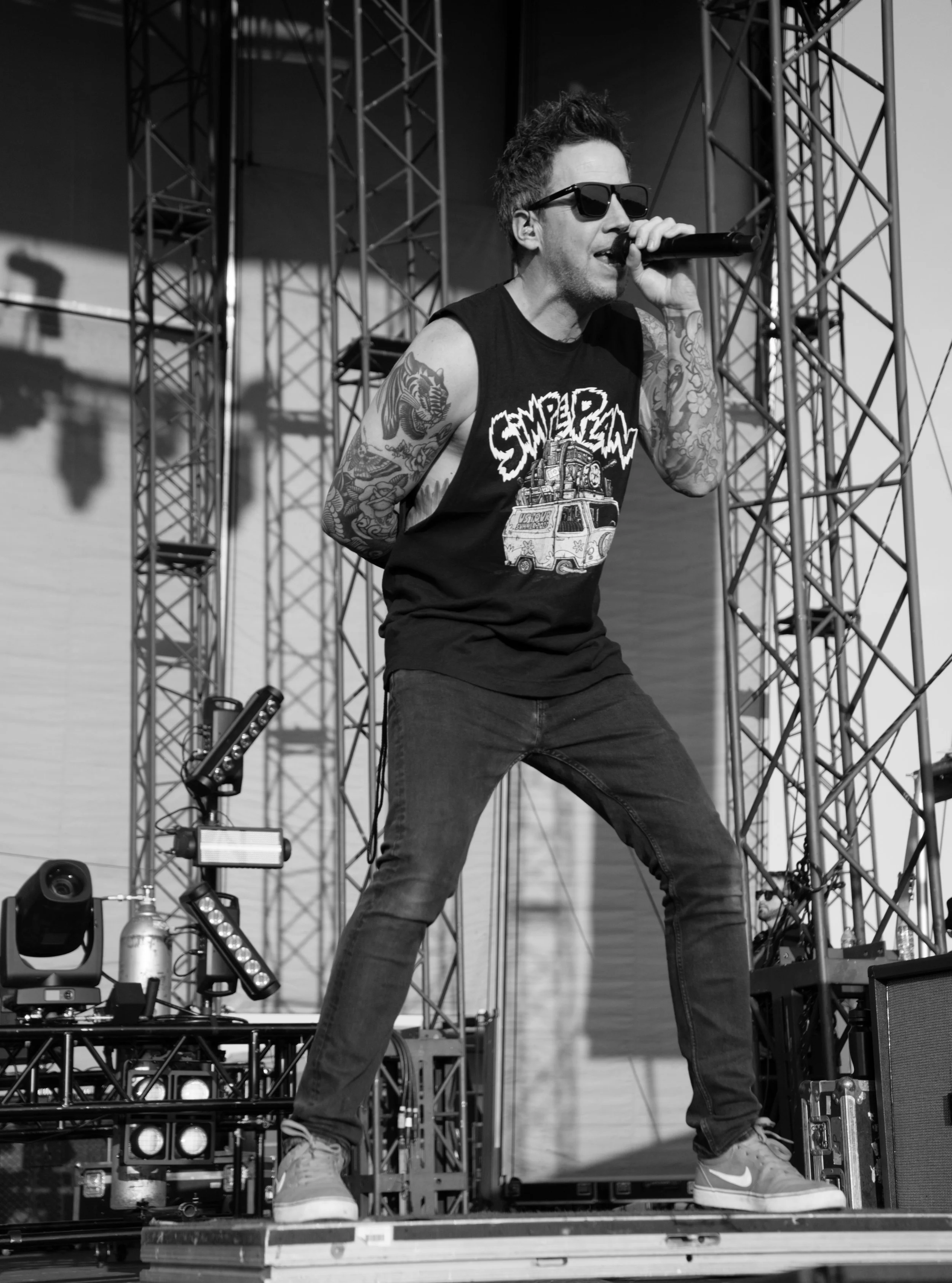 Singing performer with tattoos and sunglasses on stage with Simple Plan t-shirt.