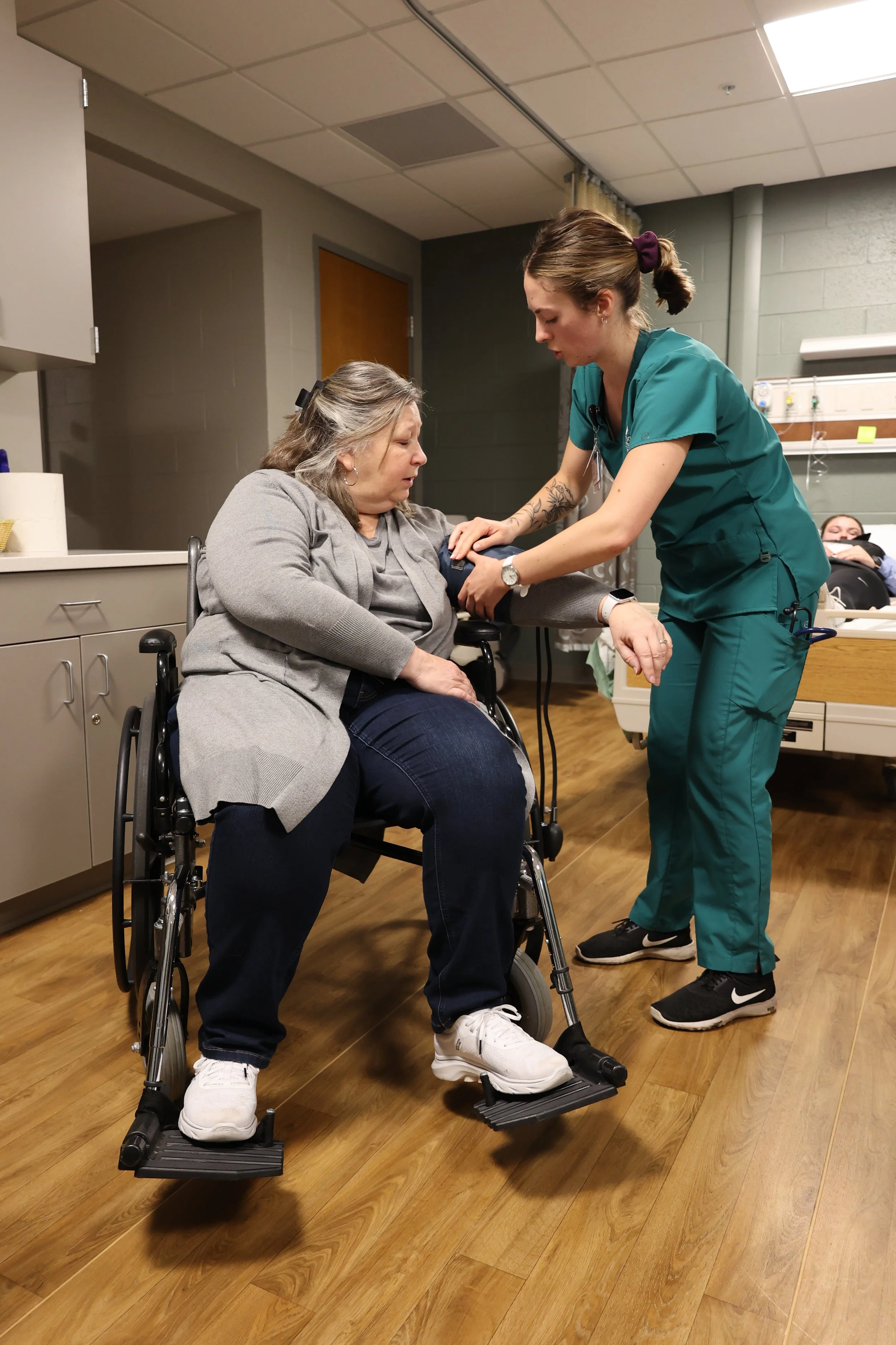 A nurse in scrubs assisting a woman in a wheelchair