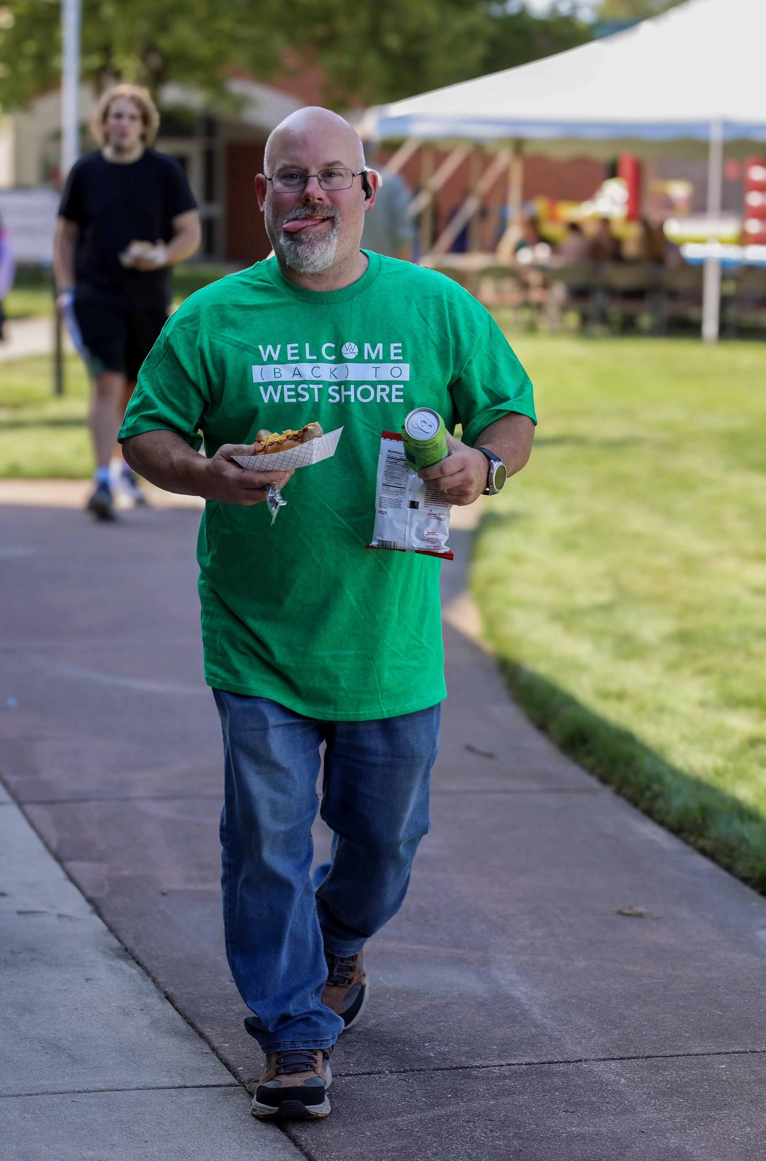 Man in green shirt walking with snacks at outdoor event.