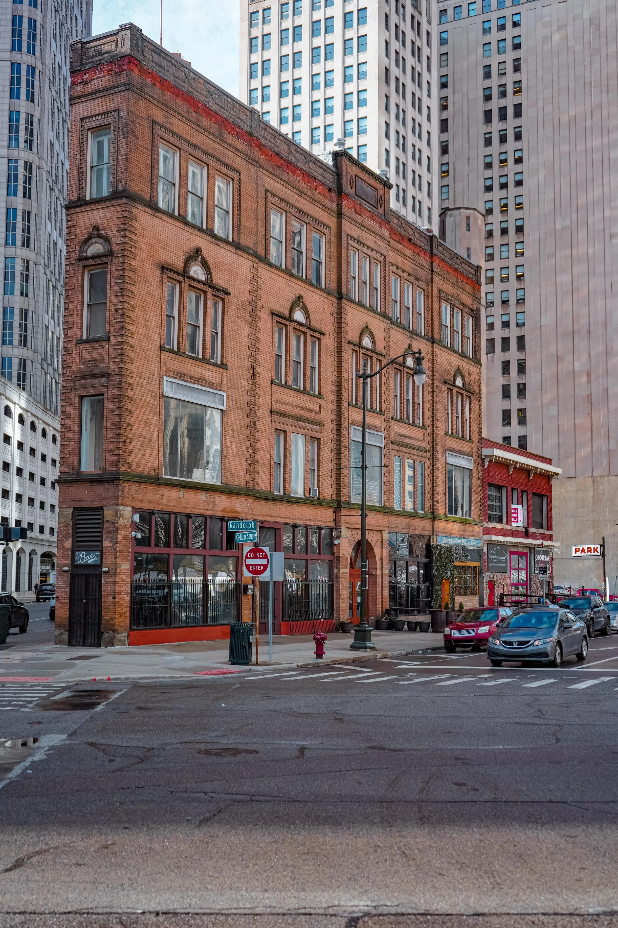 Historic brownstone building on a city street corner with cars parked alongside and a "Do Not Enter" sign at the intersection in an urban environment.