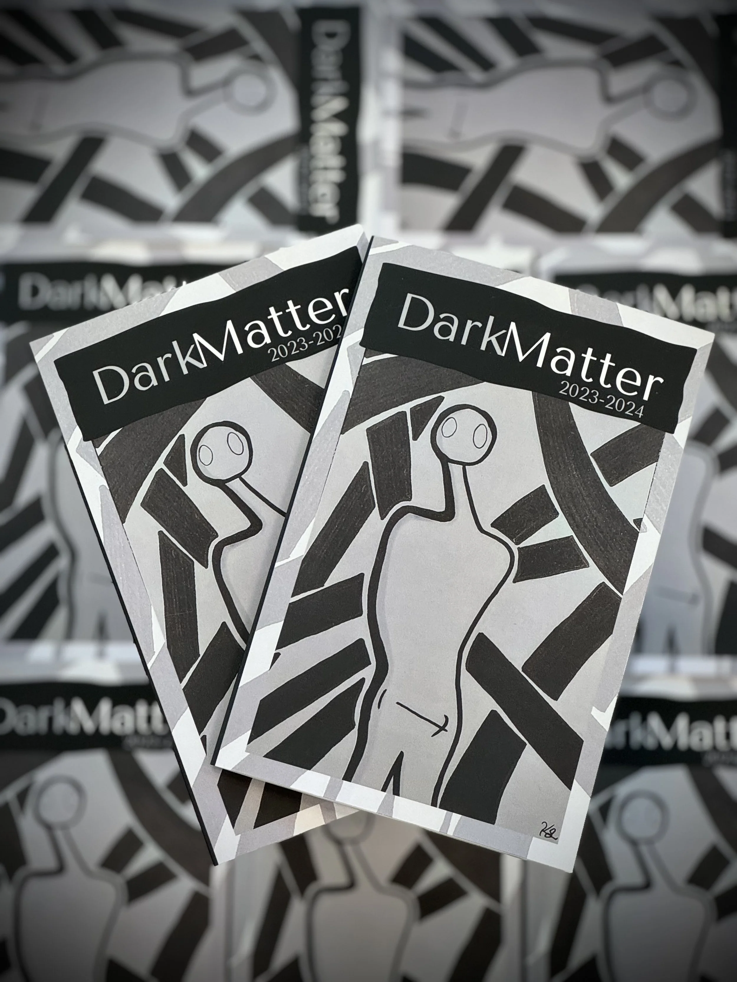 Magazines titled "Dark Matter 2023-2024" with abstract black and white covers featuring a stylized human figure.