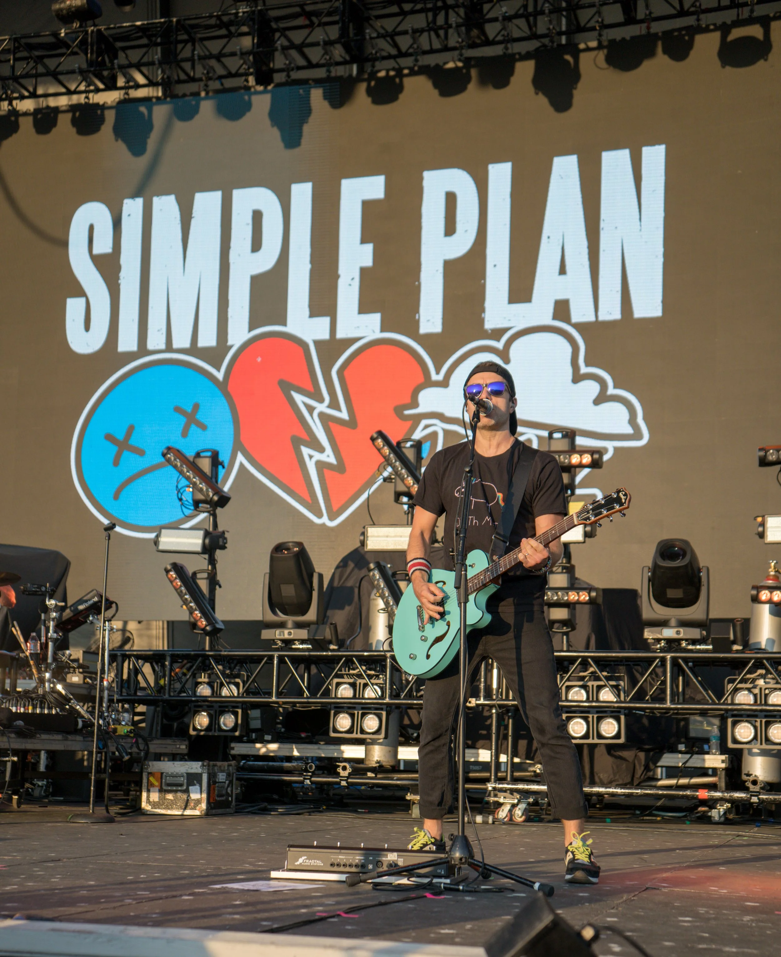 Musician on stage with a guitar performing in front of a "Simple Plan" band backdrop.
