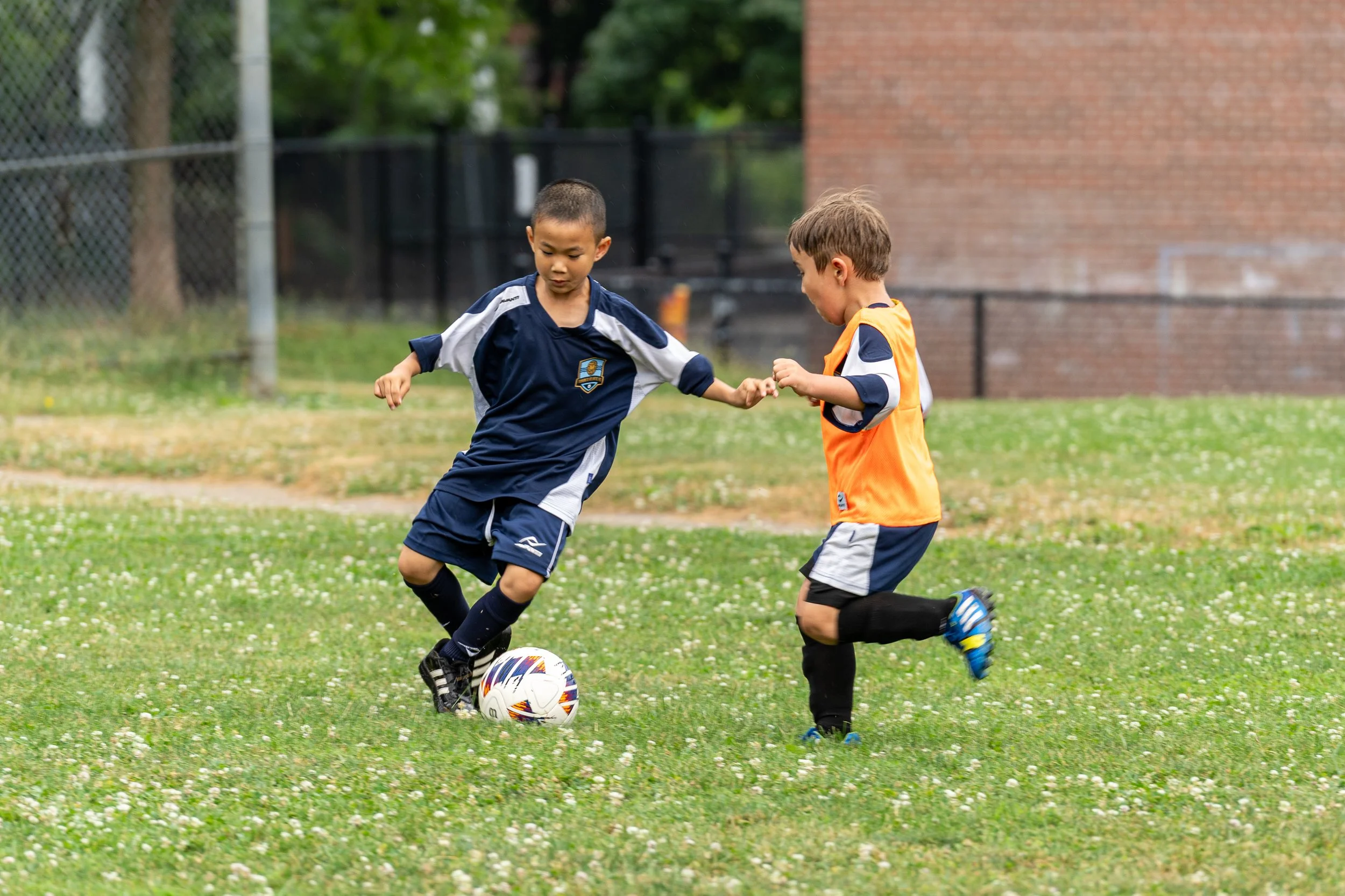 A happy family smiling on a soccer field, with a child sitting on the mother's shoulders holding a soccer ball, representing a fun and welcoming atmosphere at Toronto Atlantic FC, a youth soccer club in Toronto.