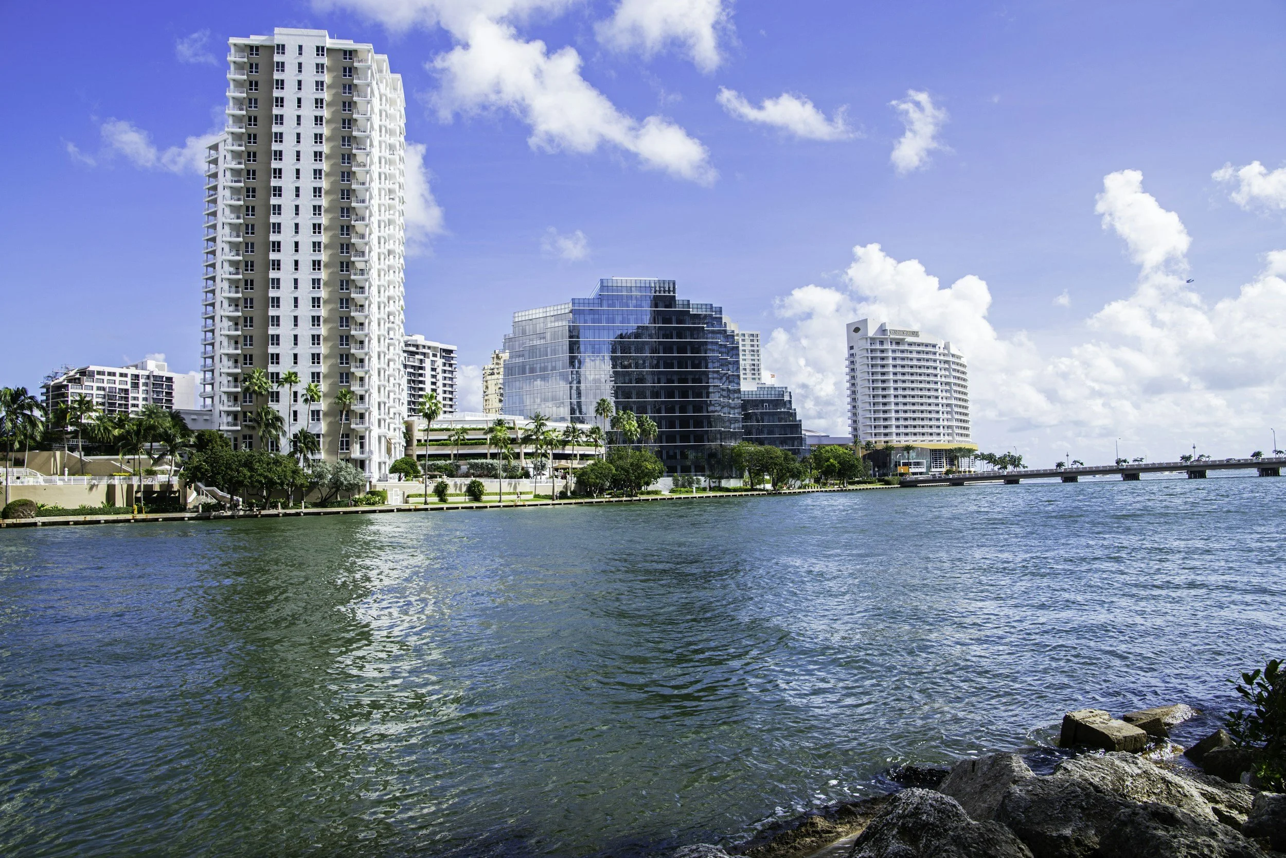 Cityscape with modern high-rise buildings along a waterway under a partly cloudy sky.