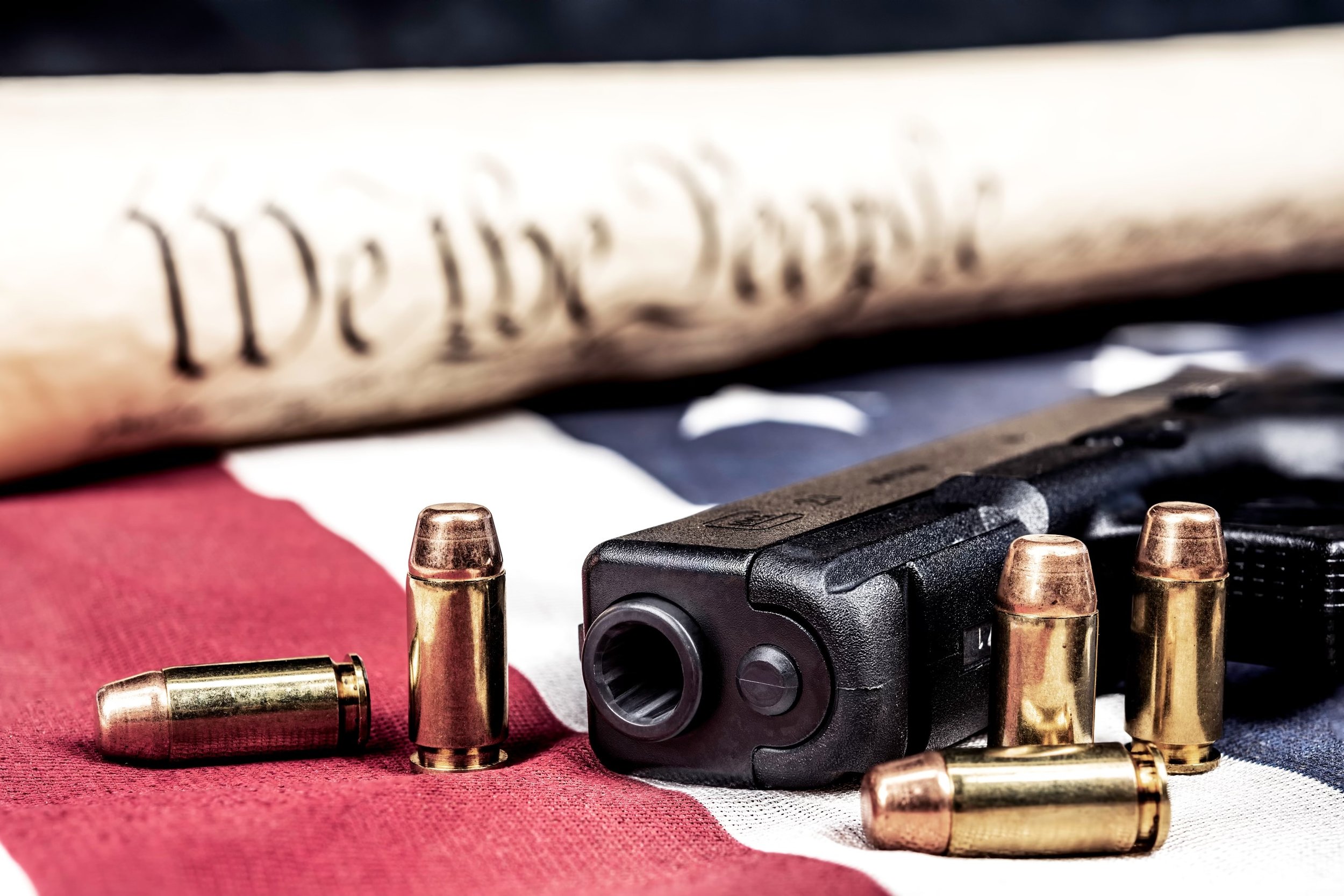 A handgun with several bullets and a rolled dollar bill on an American flag background.
