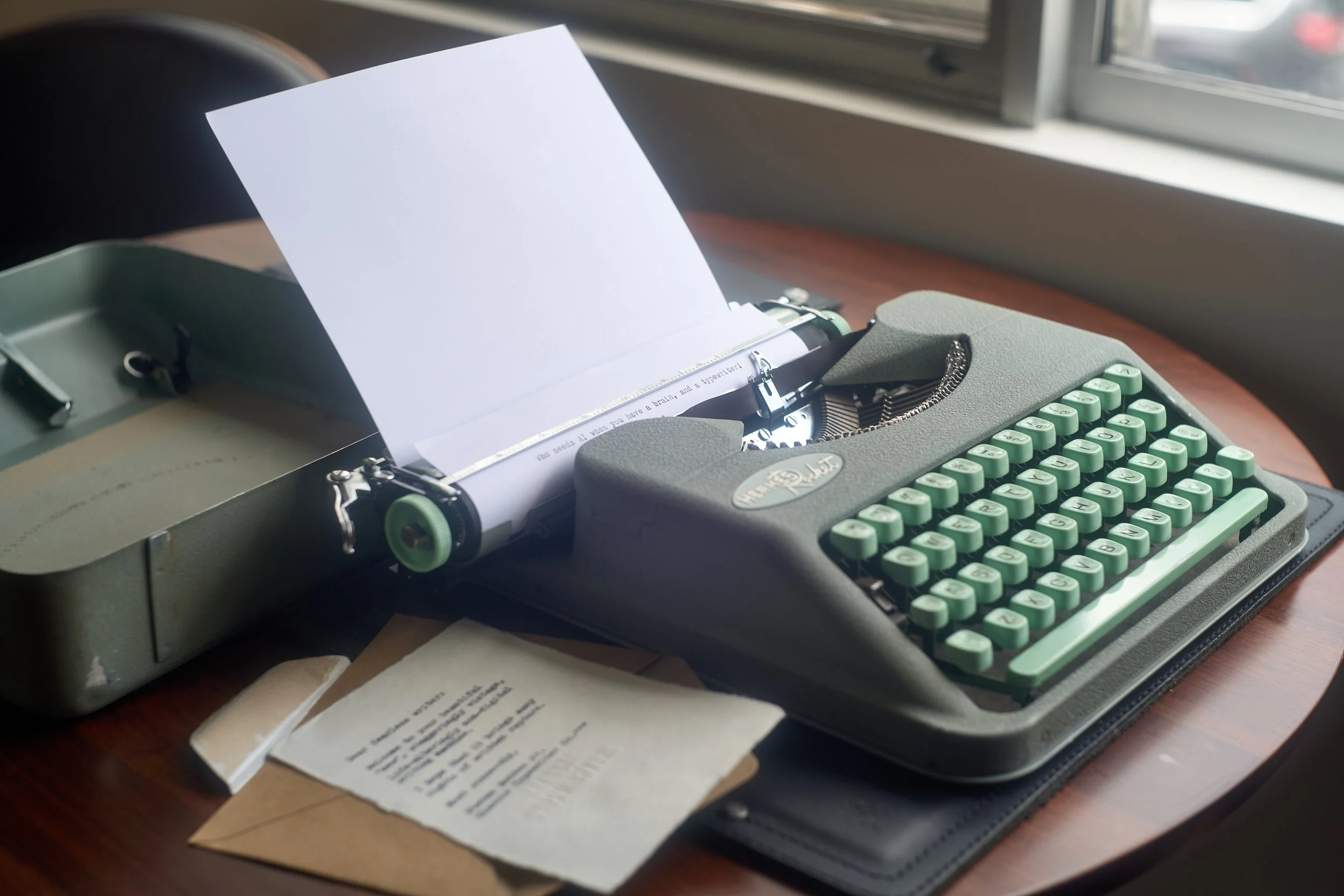 A vintage 1958 Hermes Rocket typewriter with a sheet of paper inserted, placed on a desk near a window. One paper is typed, "Who needs AI when you have a brain, and a typewriter!"