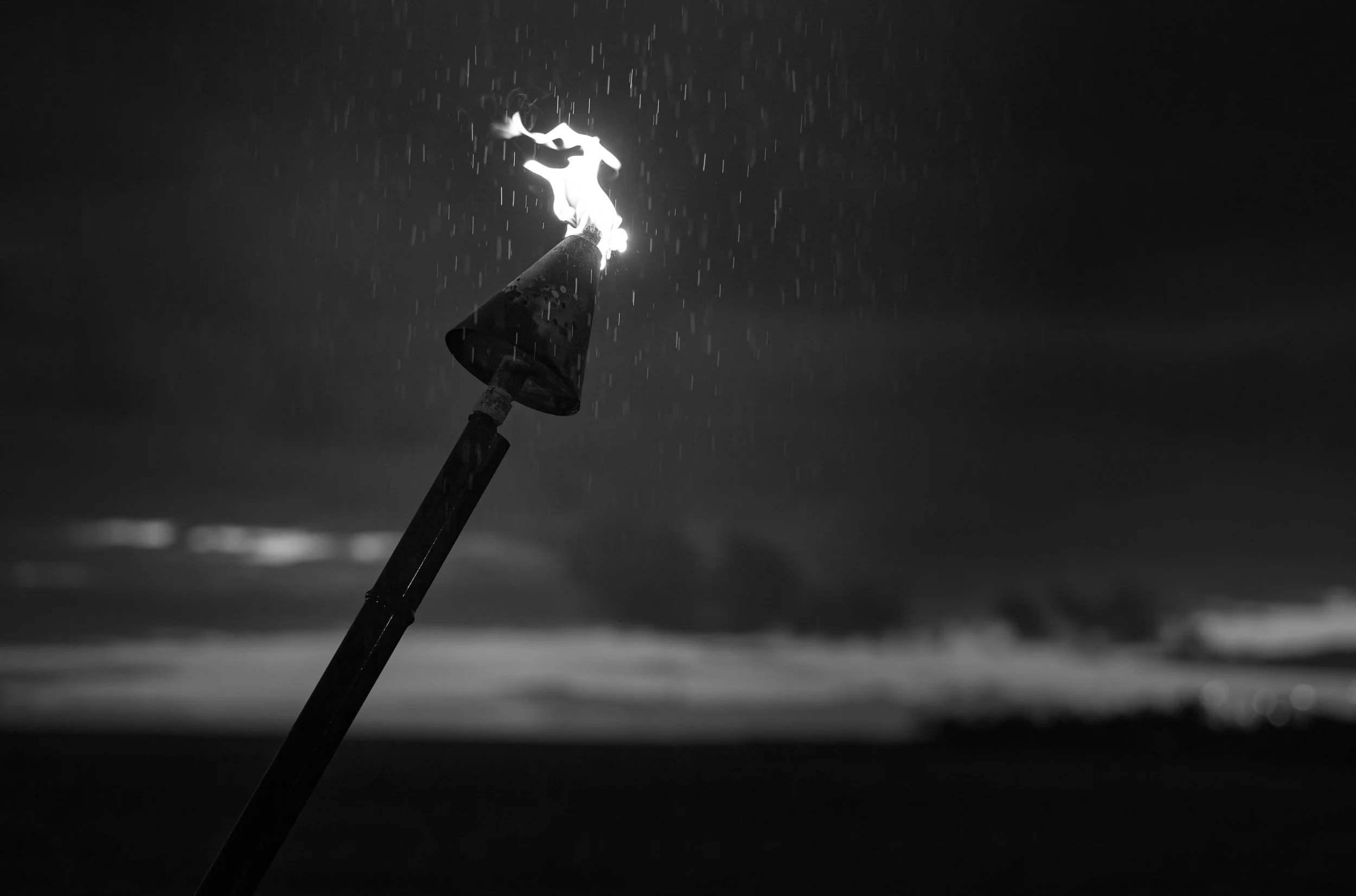 A lit fire torch with flames and sparks against a dark background, possibly at night or in low light. Kona, Hawaii.