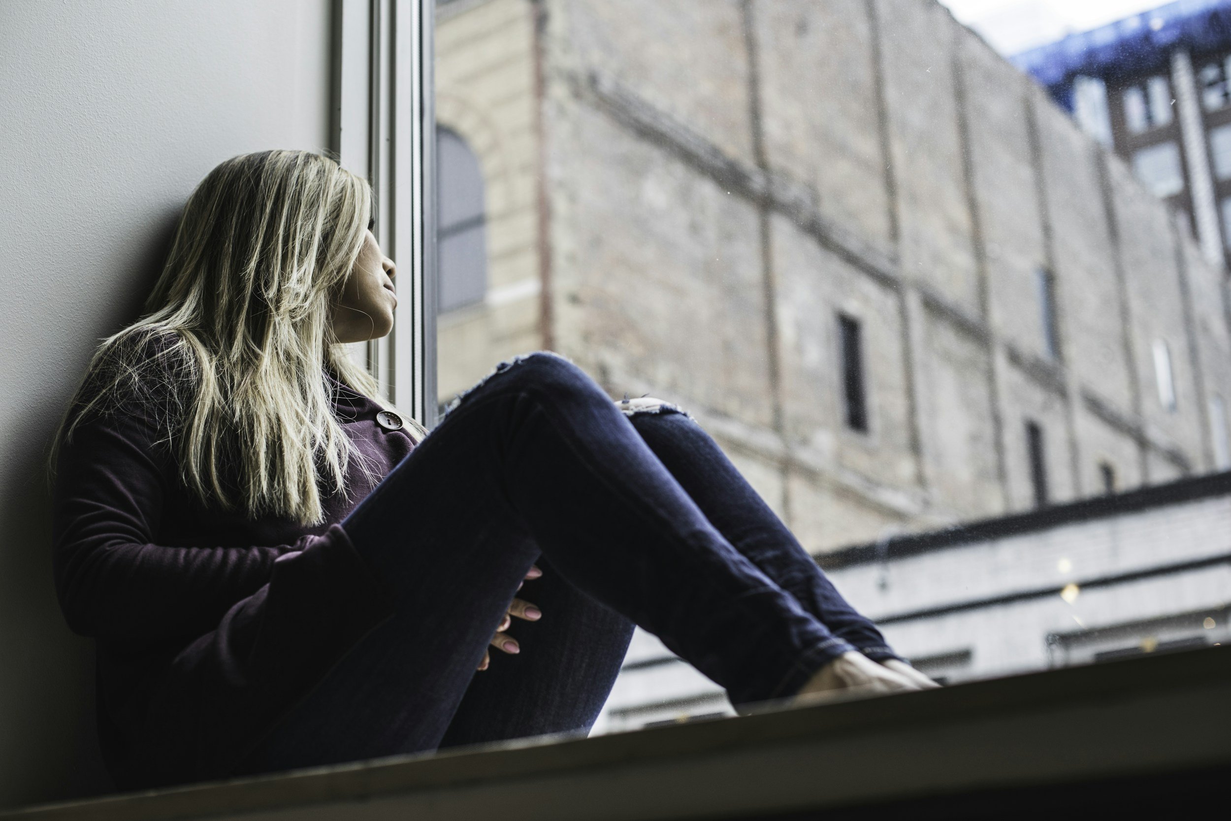 Person with long hair looking out a window inside a building.