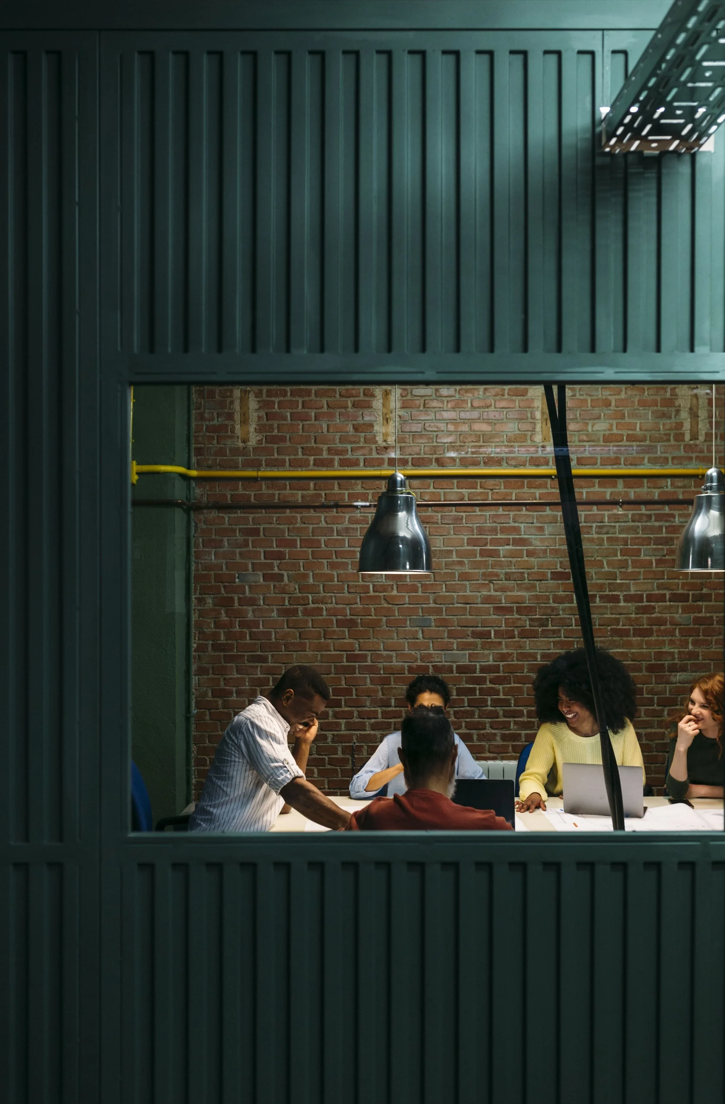 A group of five diverse people having a meeting in a modern conference room with a brick wall background, divided by green-painted panels. Career Coaching Services