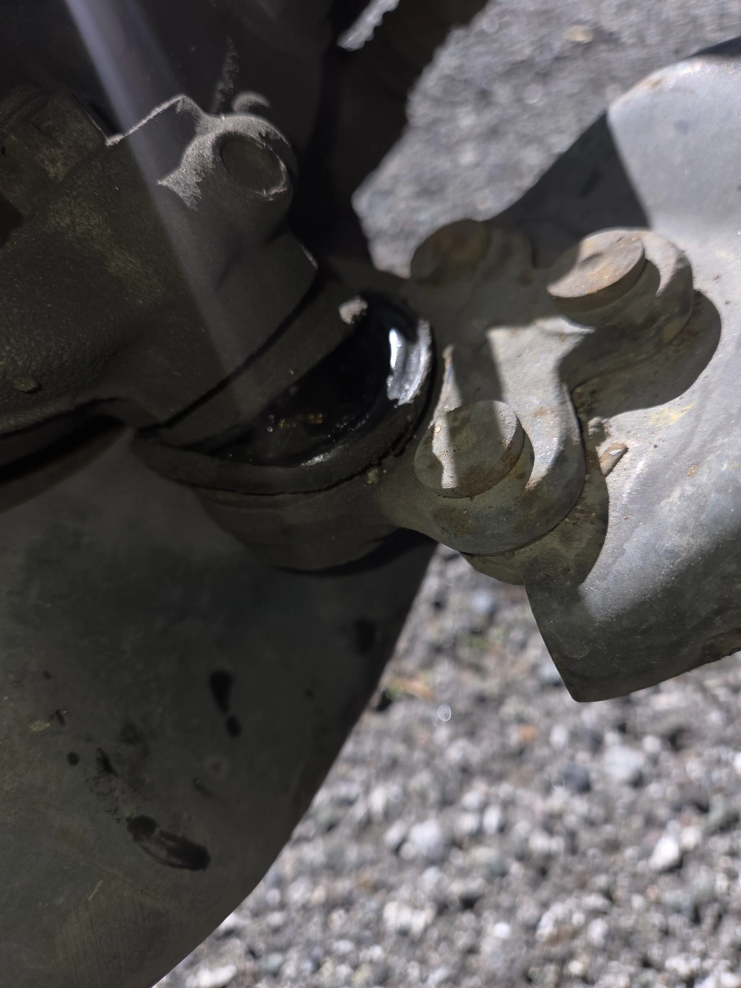 Close-up view of a mechanical part with a black oil seal on a metal surface, possibly part of a vehicle's engine or machinery, with visible bolts and a shadow cast on the surface.