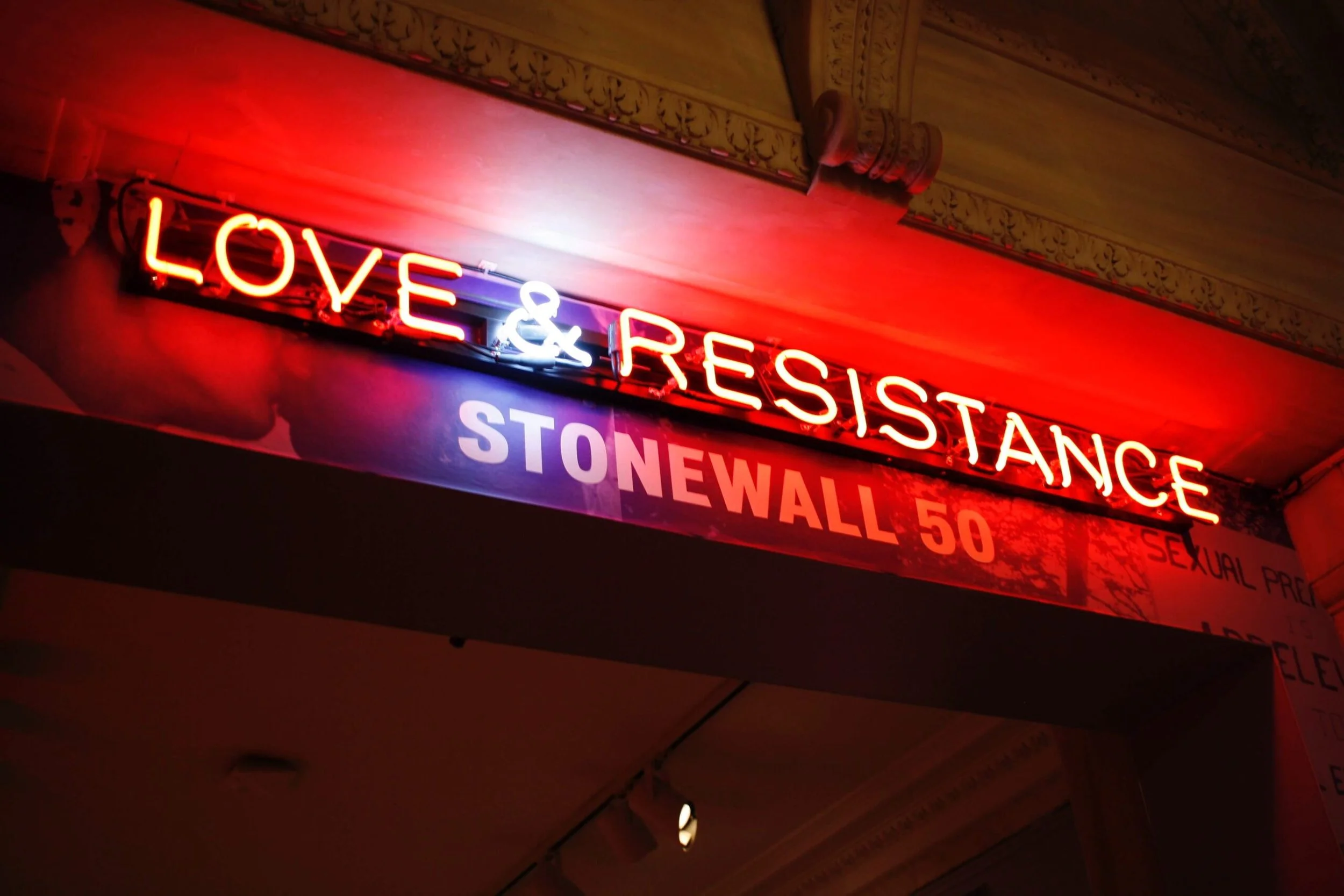 A neon sign that reads "Love and Resistance" over a banner that reads "Stonewall 50"