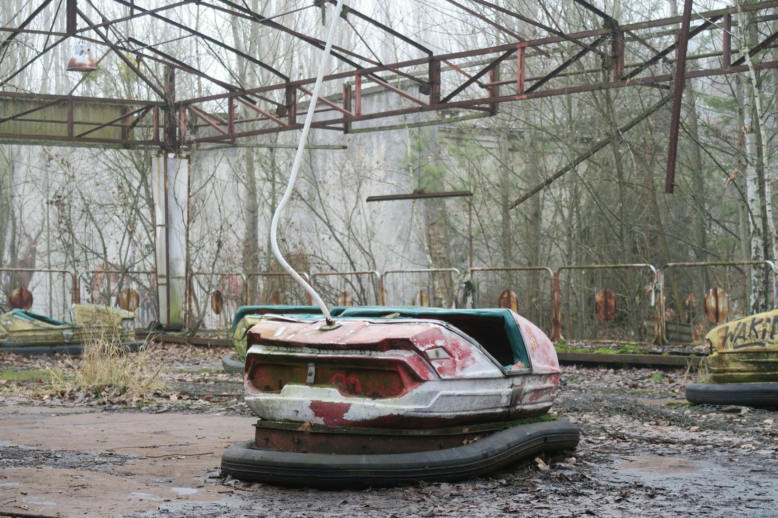 Old, abandoned bumper car in a rusty amusement park ride area surrounded by leafless trees.