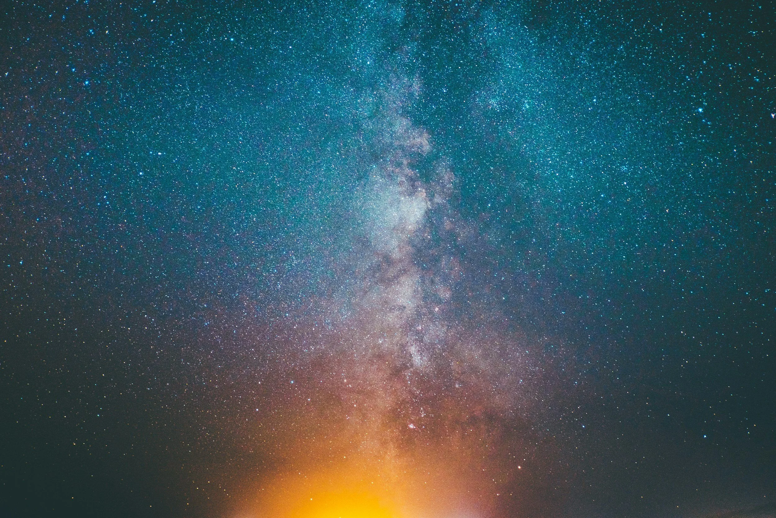 Night sky filled with stars and the Milky Way galaxy visible, with a faint glow of sunrise or sunset at the horizon.