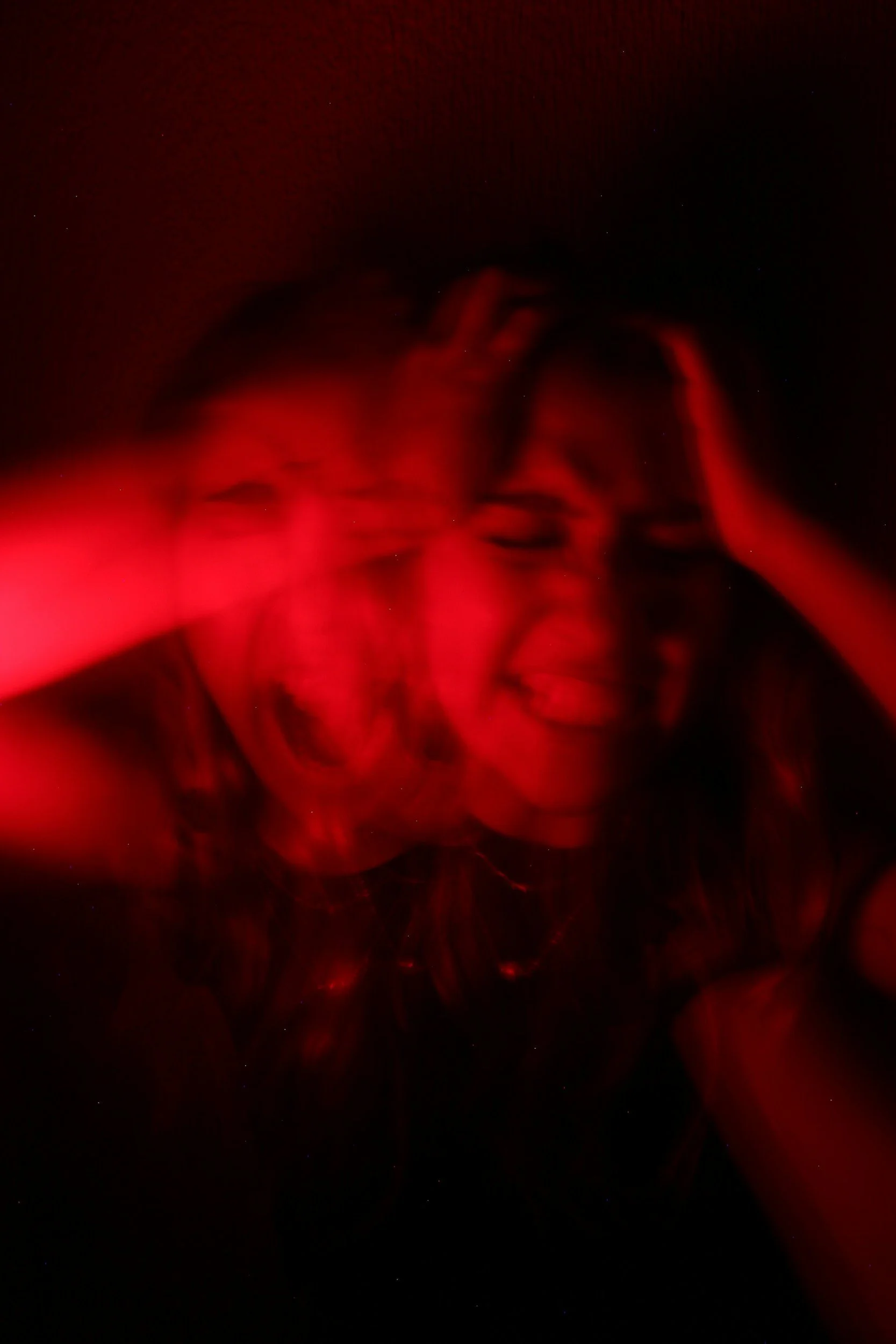 A woman in pain or distress holding her head, illuminated by red light, with a dark background.