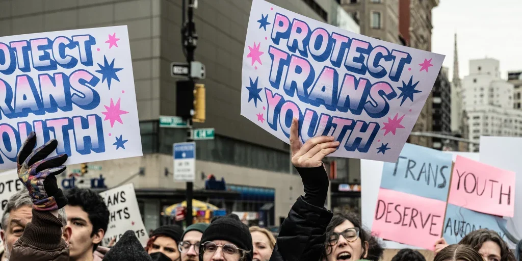 A sign reading "PROTECT TRANS YOUTH" held above a crowd of people