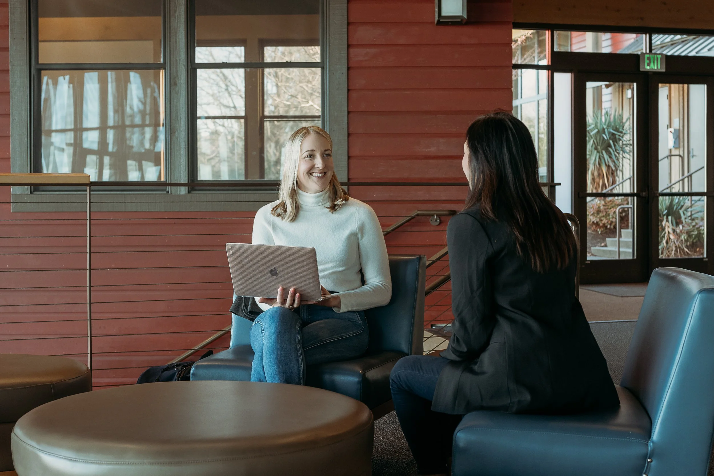 woman holding laptop smiling and talking to another woman