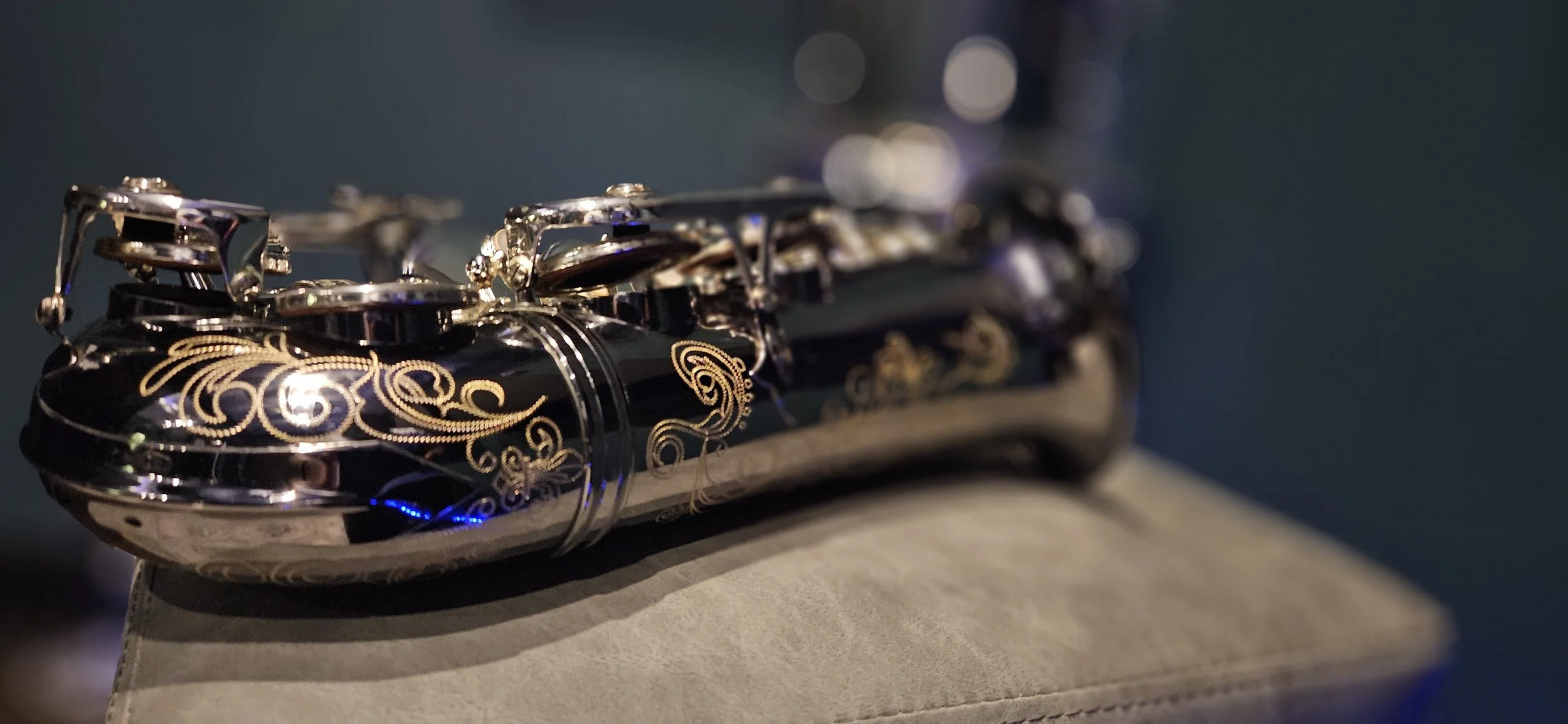 Close-up of a shiny, black flute with gold decorative patterns resting on a beige surface.