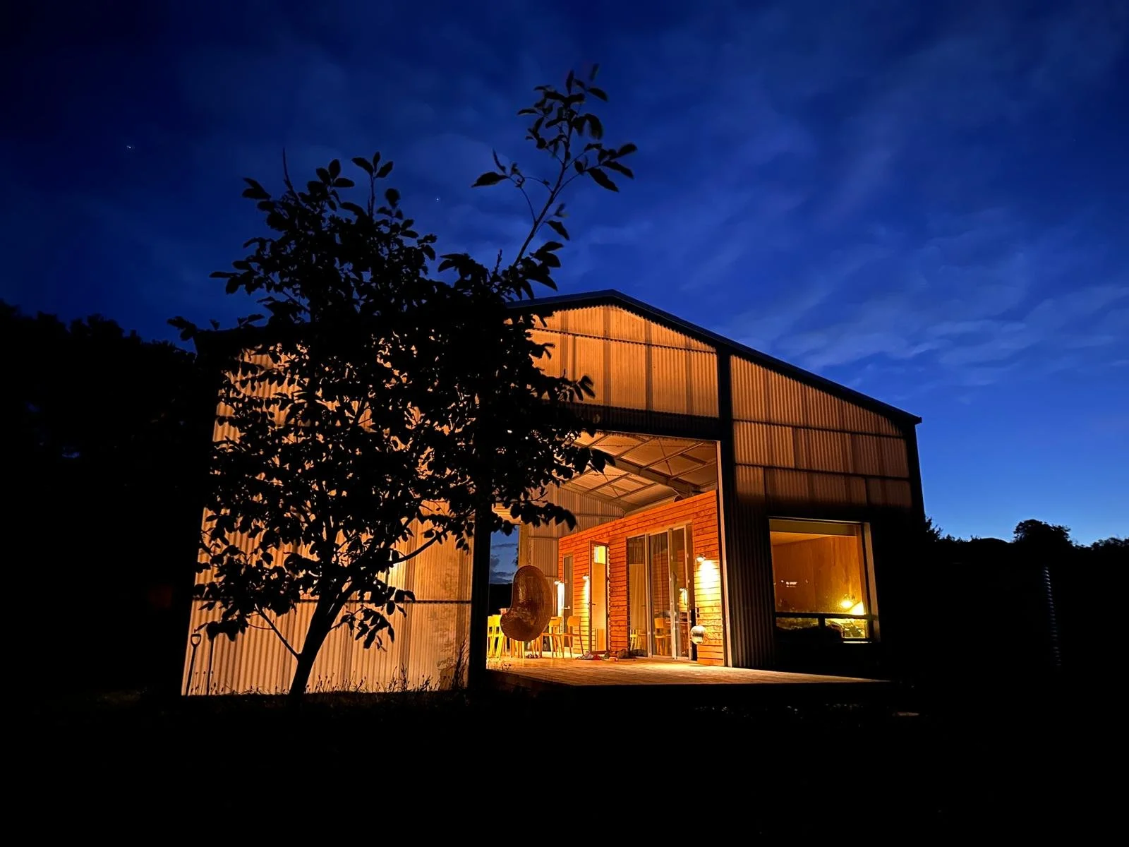 A contemporary home designed by Patchwork Architects using transluscent cladding and timber pods for living either side of a large deck set against the night sky.