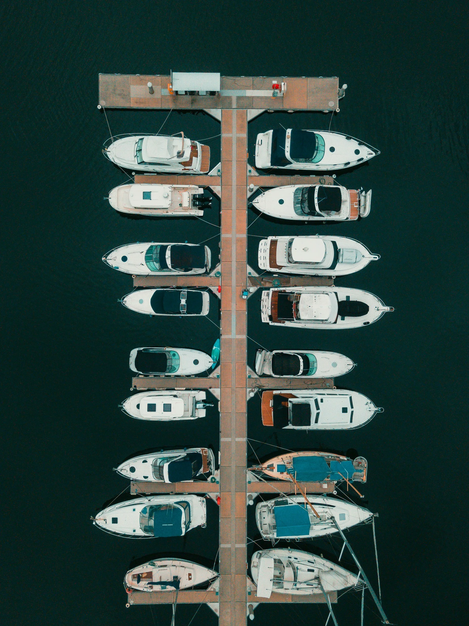 Aerial view of a marina with multiple boats docked along a pier in calm water.