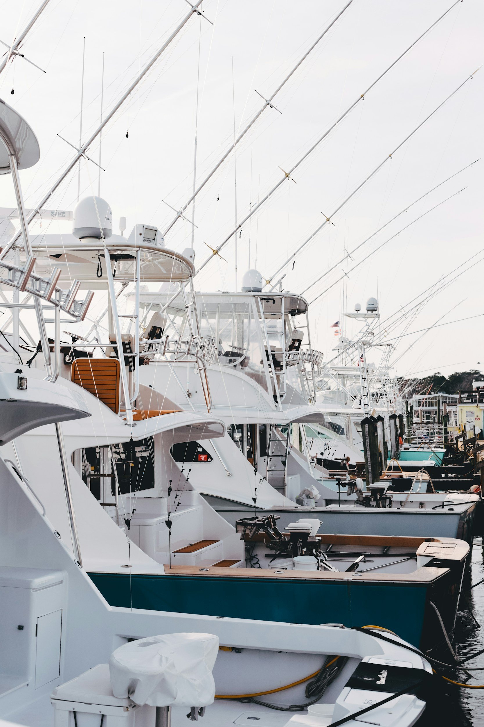 Several white yachts docked at a marina, with fishing rods extending from their decks and various equipment visible.