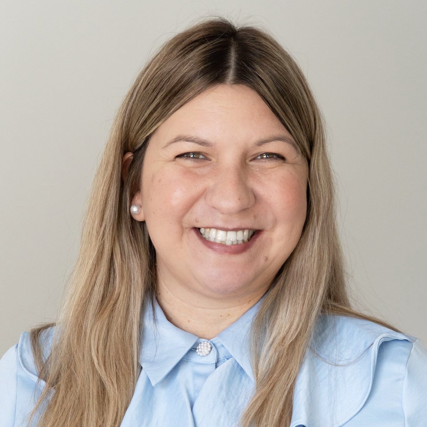 Retrato de uma mulher sorridente com cabelo castanho e lisa, usando uma blusa azul clara e brincos de pérola.