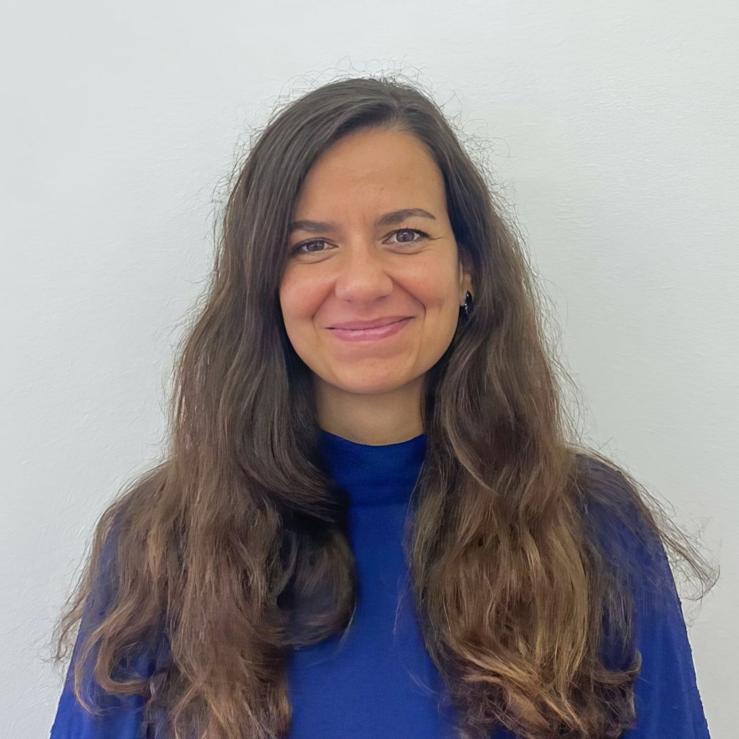 Retrato de uma mulher com cabelo castanho e comprido, sorrindo, usando blusa azul clara, contra fundo branco.
