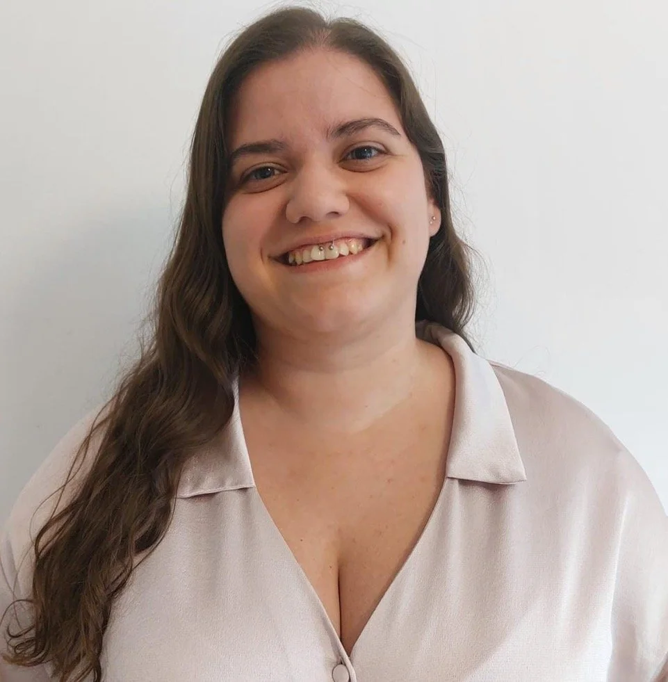 Mulher sorrindo com cabelo castanho, usando blusa clara, contra fundo branco.