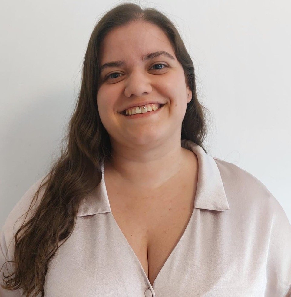 Mulher sorrindo com cabelo castanho, usando blusa bege, contra fundo branco.
