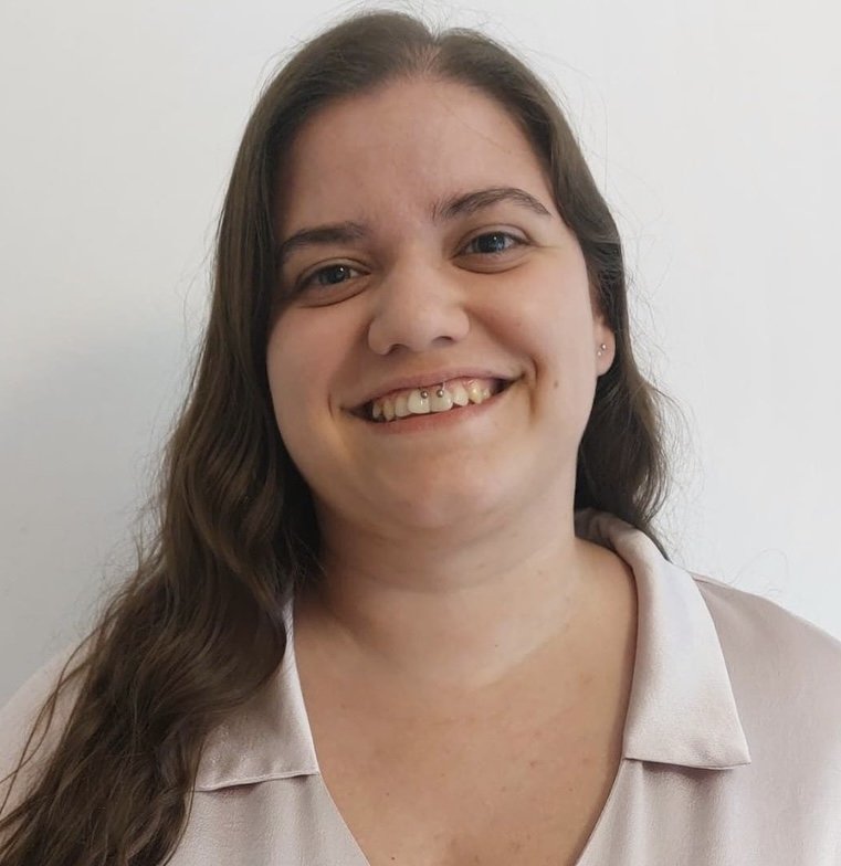 Retrato de uma mulher com cabelos cacheados, sorrindo, vestindo uma camiseta bege, contra fundo branco.