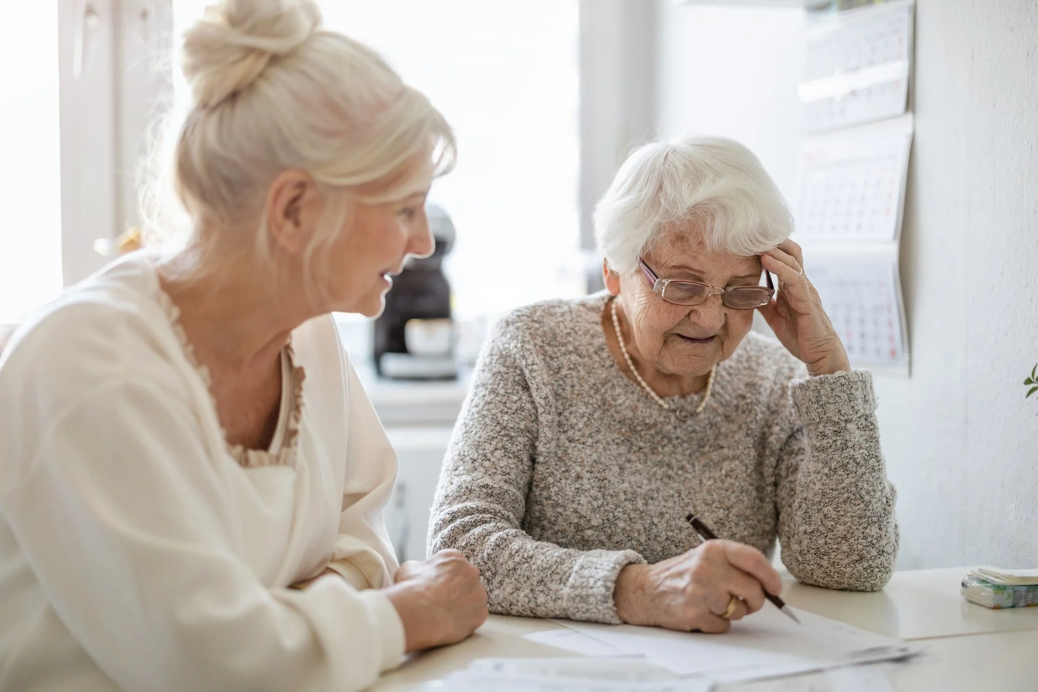 An older woman and a younger woman sit together at a kitchen table, reviewing paperwork in a bright, naturally lit home. The image reflects family support and the importance of having guidance when navigating estate planning and probate matters.