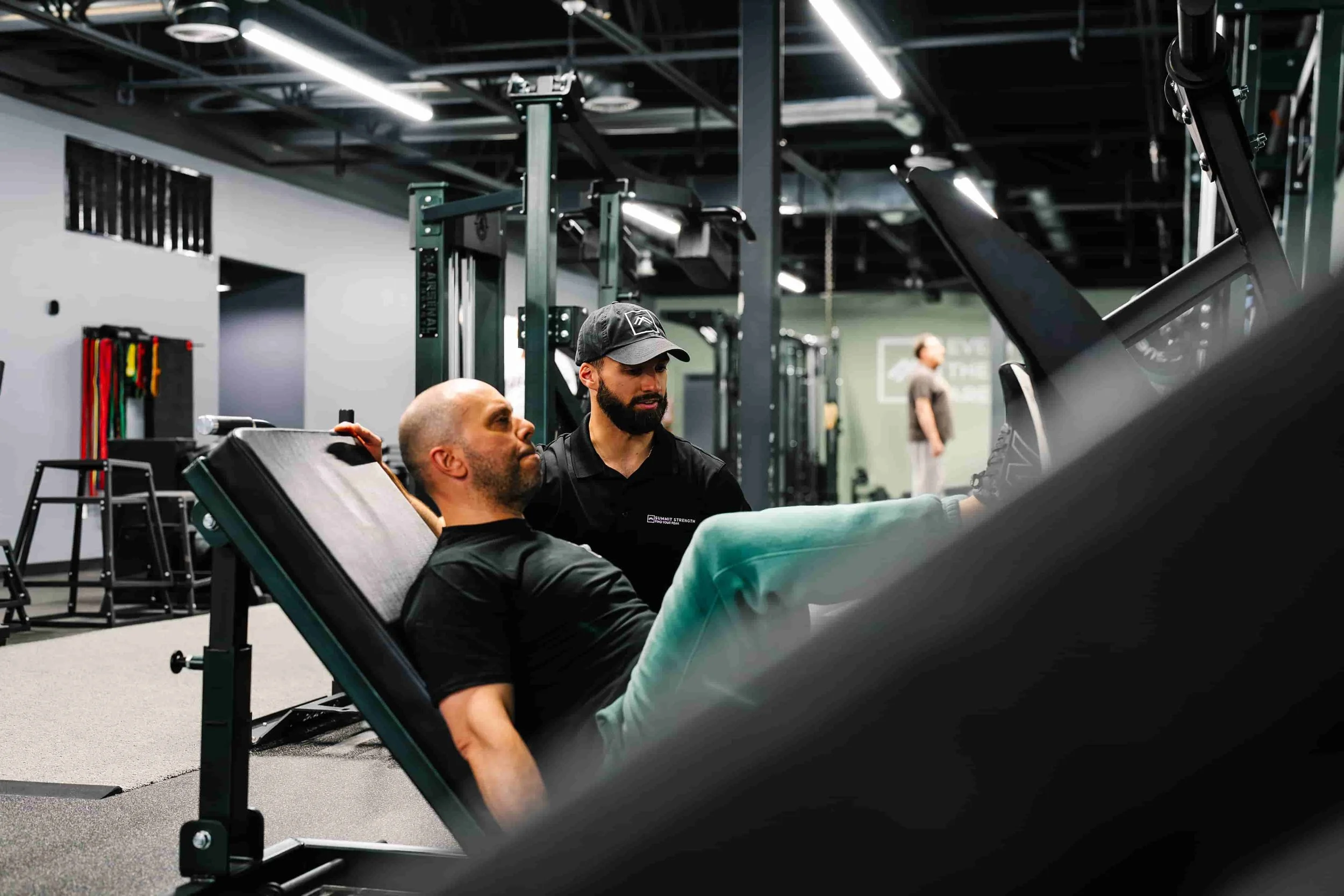 A personal trainer attentively coaching a male client performing a leg press machine exercise at a fully equipped private training gym in Milford, New Hampshire