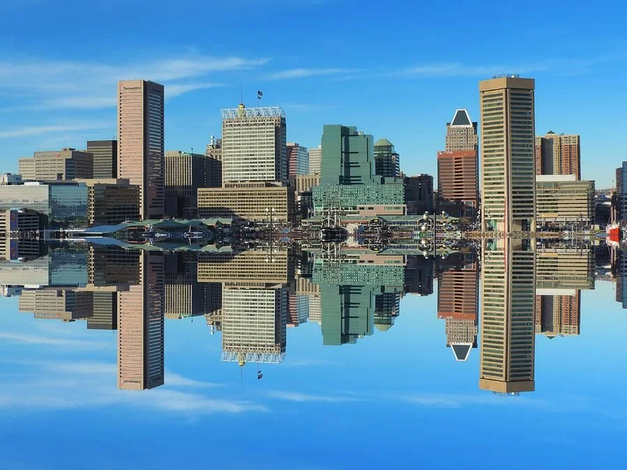 City skyline with tall buildings reflected in water under a clear blue sky.