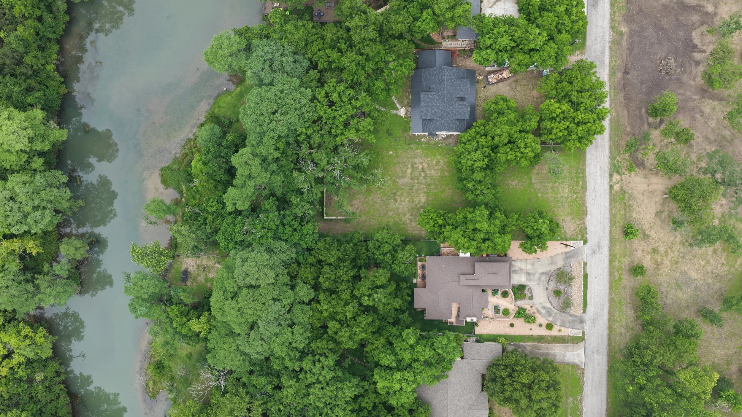An aerial view of a residential area with houses, trees, and a river on the left side of the image.