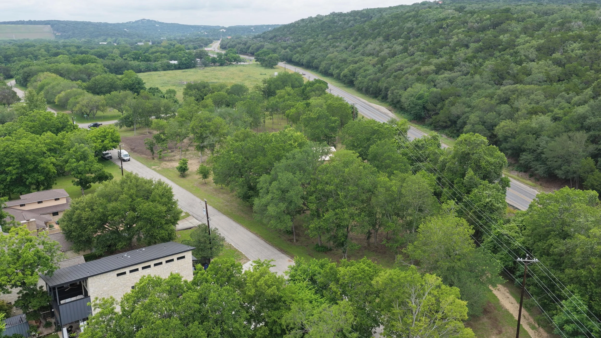 Aerial view of a green landscape with trees, roads, and hills in the background.