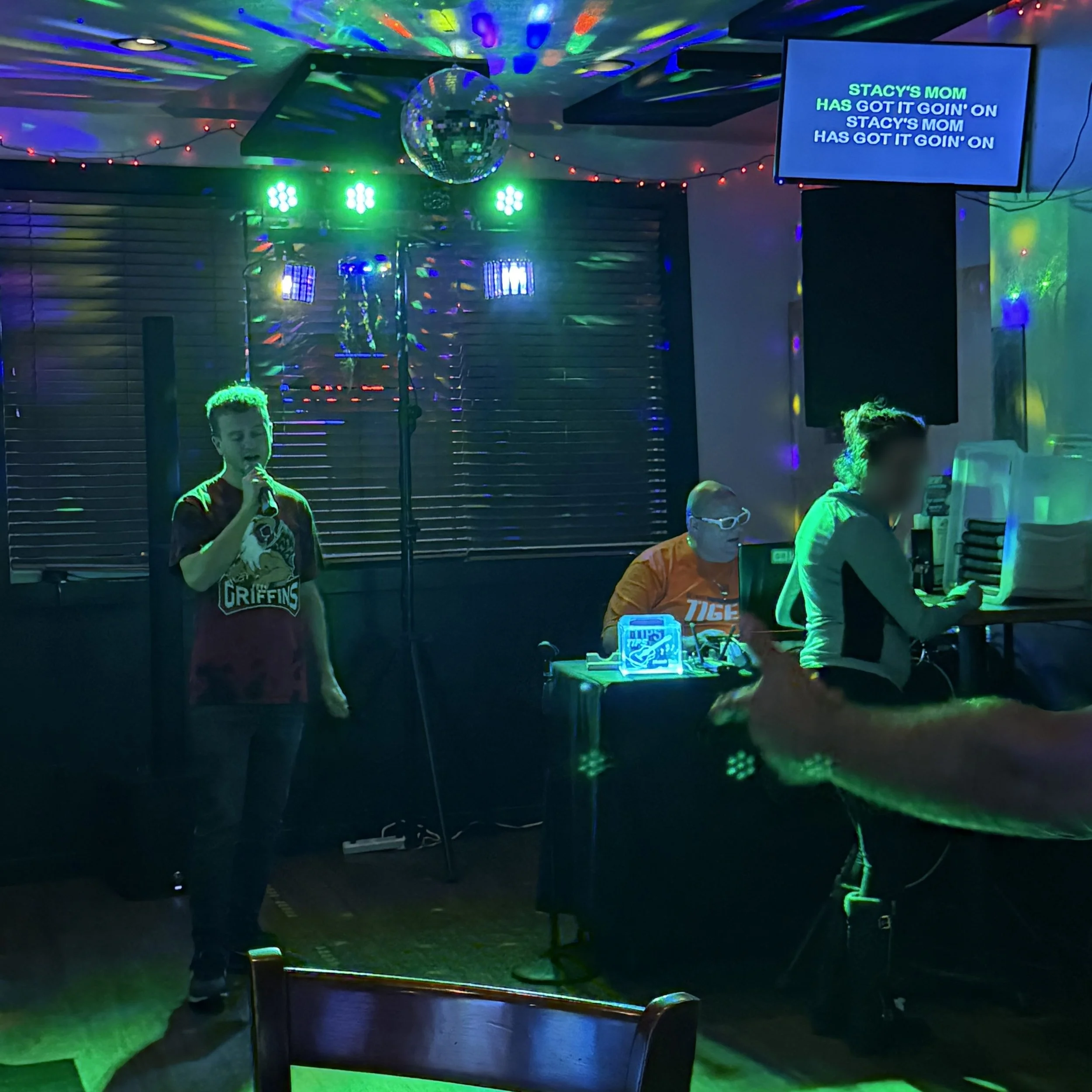 GRkaraoke.com founder Chris singing “Stacy’s Mom” at Glass House in Grand Rapids, Michigan, with karaoke host Mikey K., colorful lights, disco ball and lyric screen during the Karaoke Marathon 2026