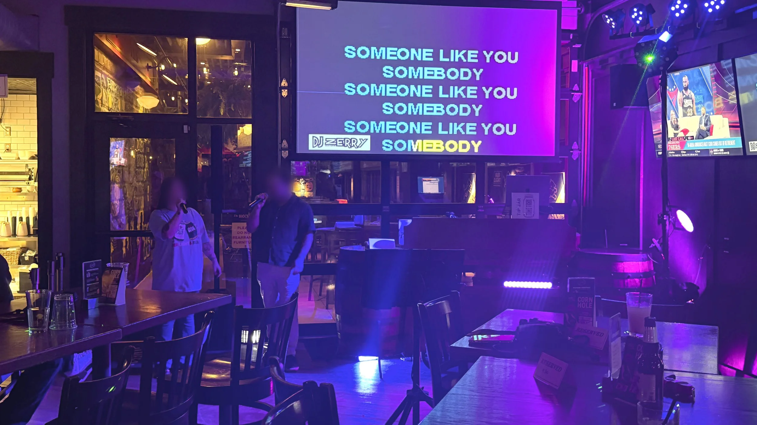 Two singers performing karaoke at The Holiday Bar on the West Side of Grand Rapids, Michigan, with colorful stage lighting and projected lyrics during the GRkaraoke.com Karaoke Marathon 2026