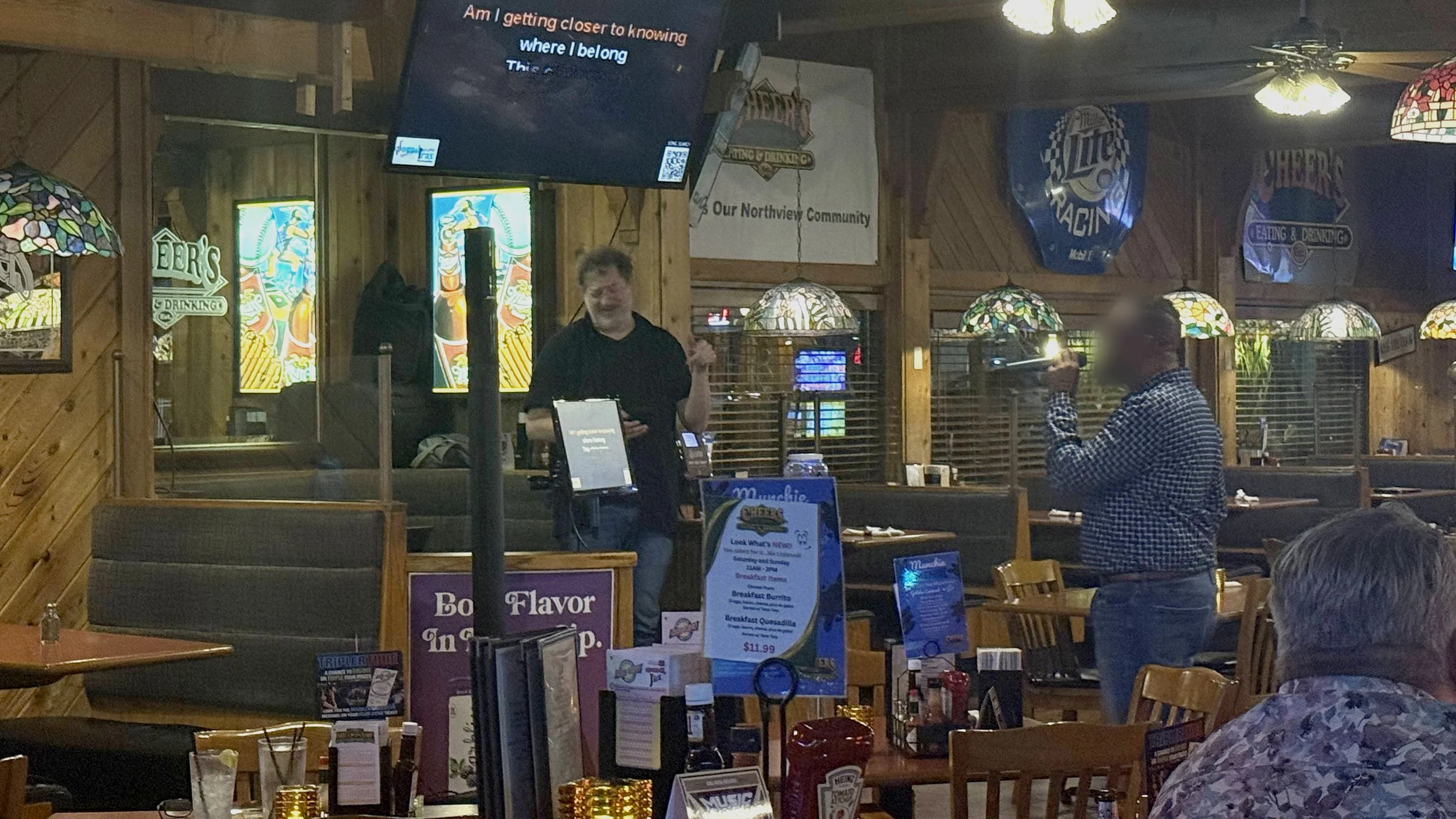 Karaoke night at Cheer’s Good Time Saloon on Plainfield Avenue in Grand Rapids, Michigan, showing a singer performing with the karaoke host and lyric screen during the GRkaraoke.com Karaoke Marathon 2026