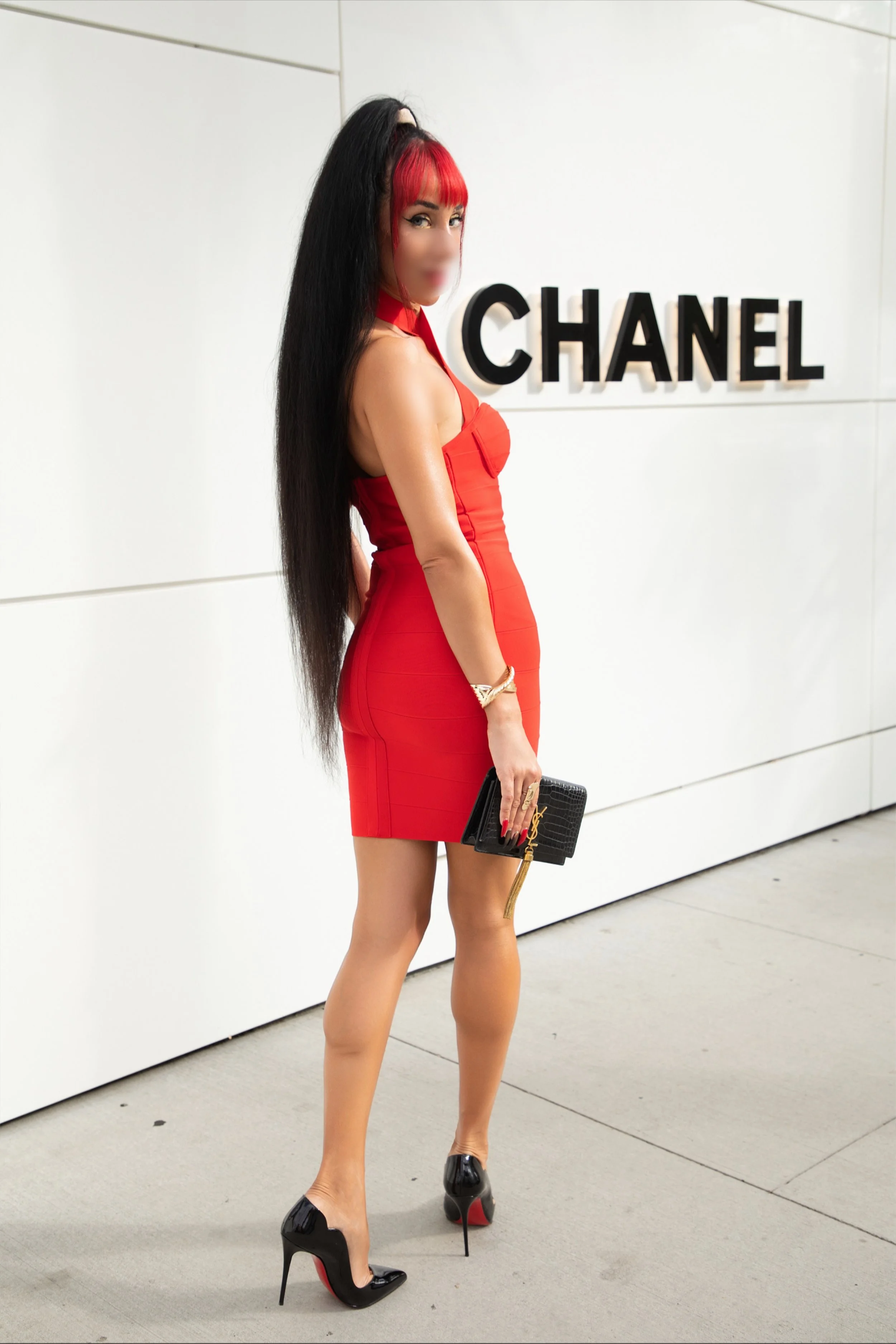 Bella Venus in a red dress and high heels stands in front of Coco Chanel. 