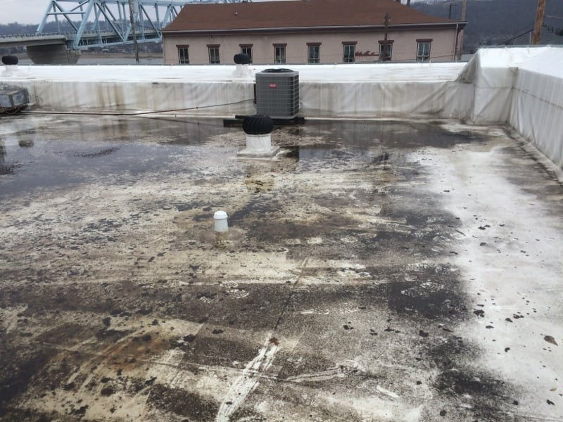A weathered white commercial rooftop showing extensive ponding water and debris buildup, a primary concern for winter commercial roof damage that requires professional intervention from Mainline Building.
