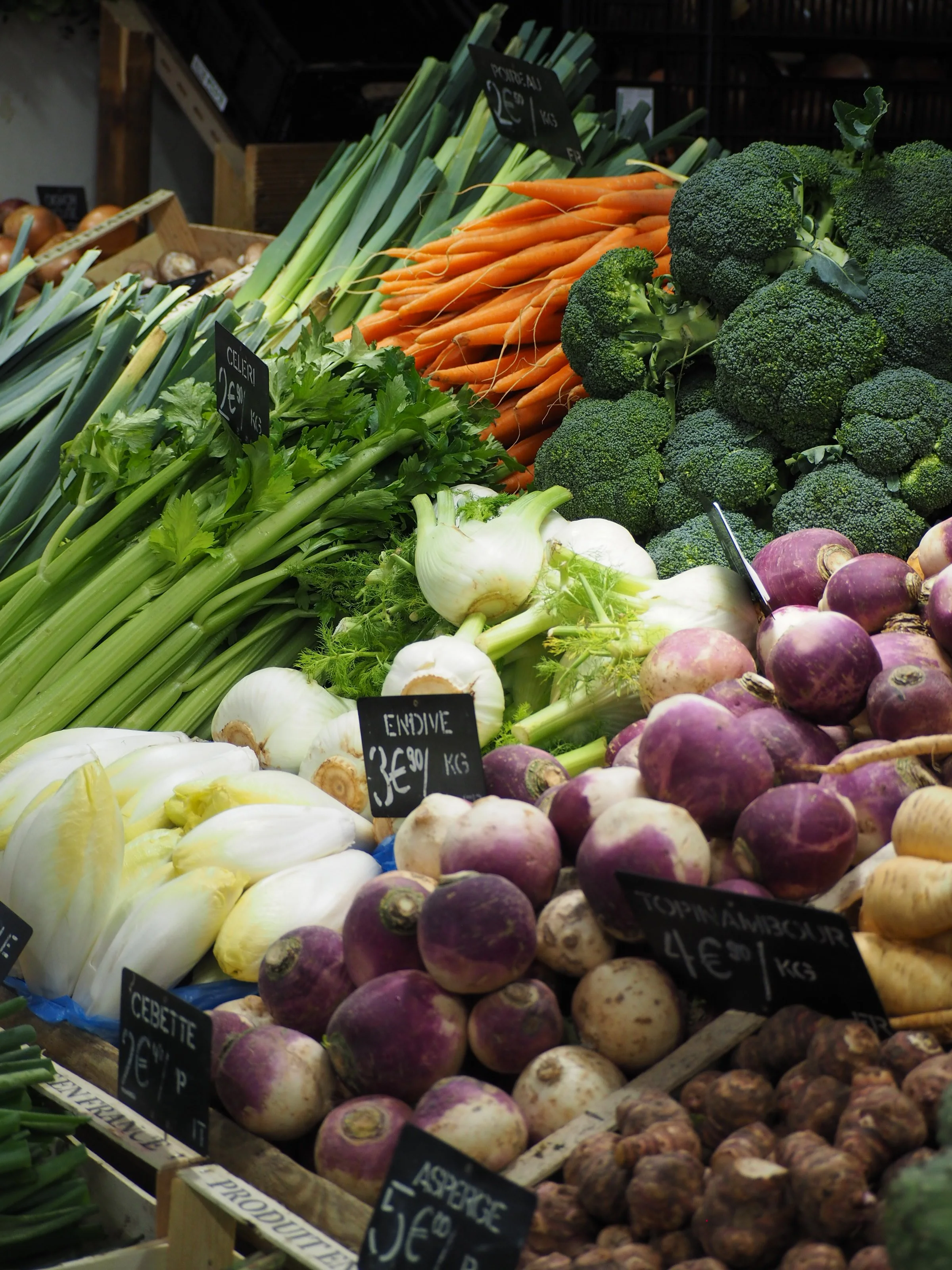 Display of fresh vegetables at a market, including carrots, broccoli, onions, and turnips.