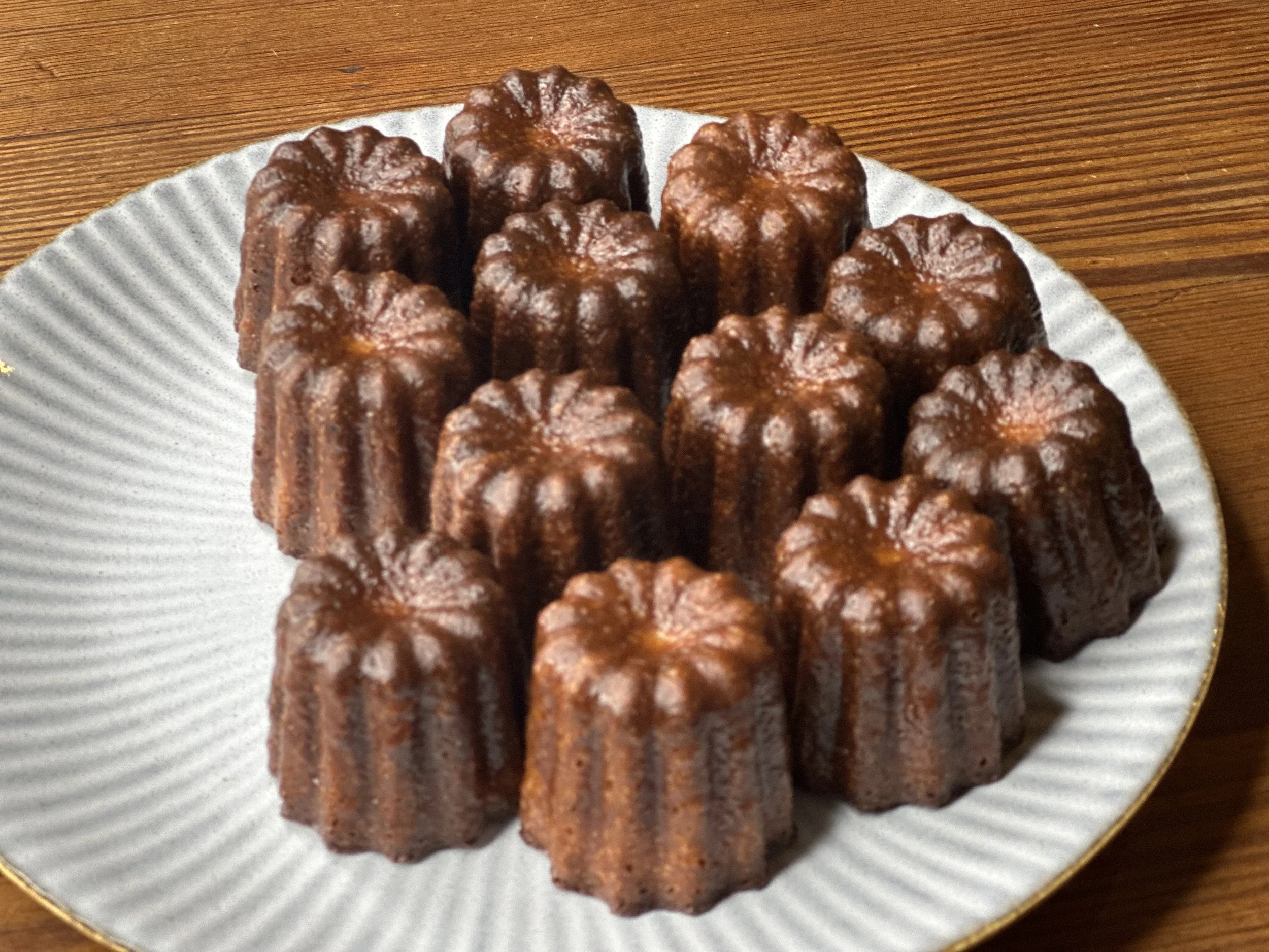 Canelé pastries on a white plate with gold rim on a wooden table.