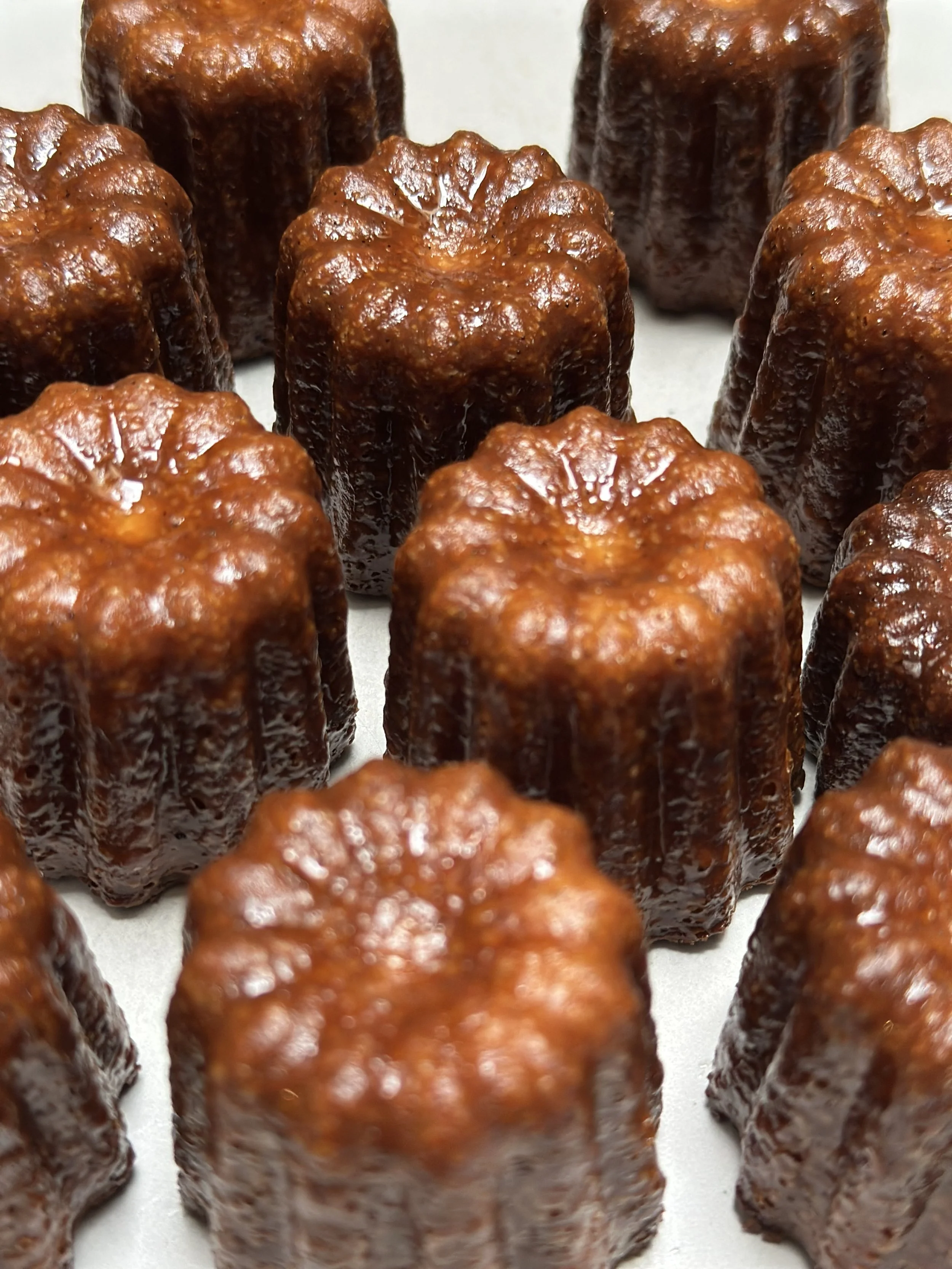 Close-up of multiple cannelés, small French pastries with a dark caramelized crust and a soft, custard-like interior.