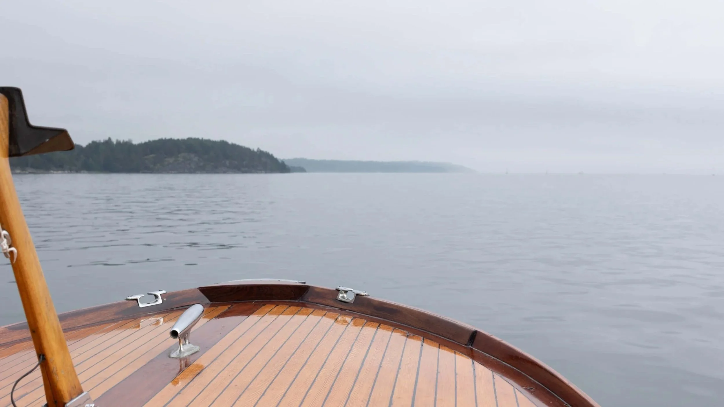 View across calm water from a wooden boat towards a distant shoreline.
