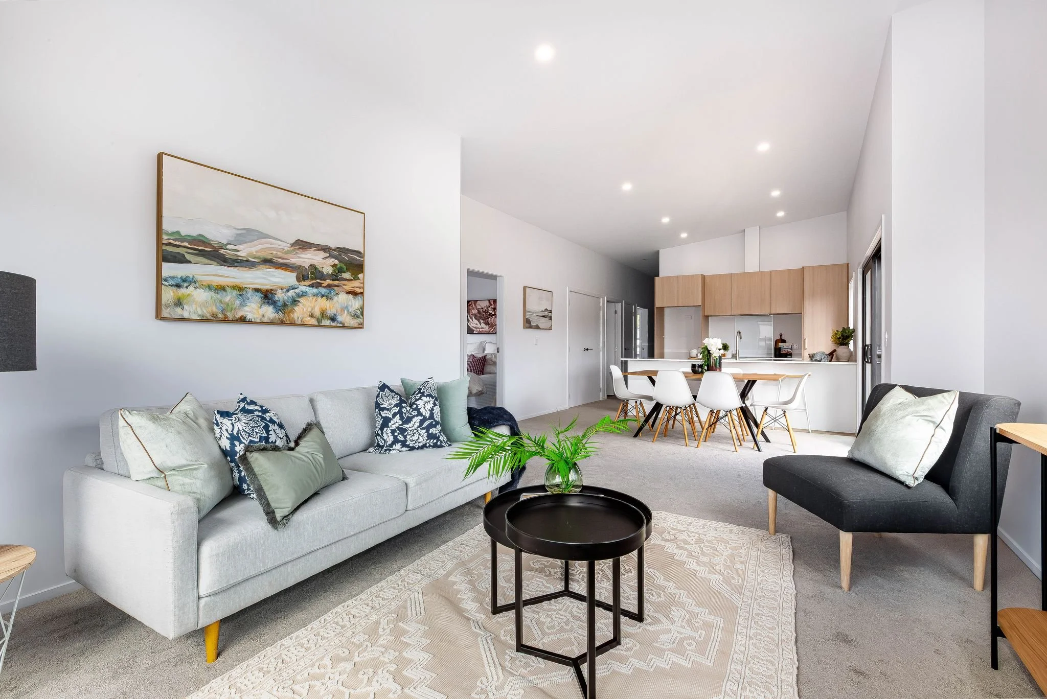 Open-concept living room and dining area with white sofa, black armchair, coffee table with plant, and a dining table with white chairs in a modern home.