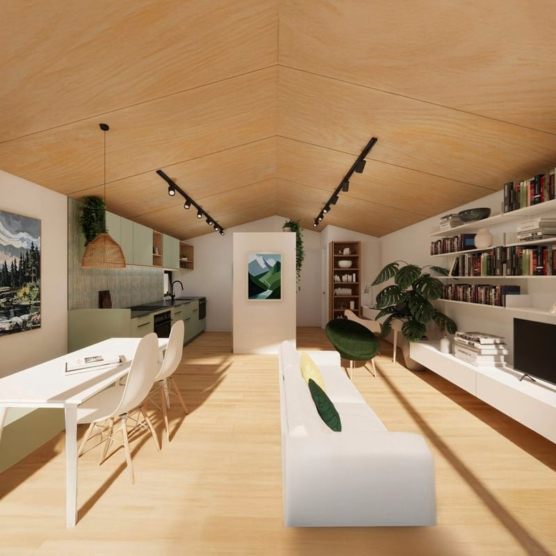 A modern, cozy living room with a vaulted wooden ceiling, white walls, and hardwood floors. The space features a white sofa with cushions, a large potted plant, a white entertainment unit with books and a TV, a dining table with white chairs, a kitch