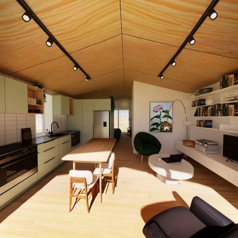 Open-concept kitchen and living space with a wooden ceiling, black track lighting, cream cabinets, a dining table with chairs, a green armchair, wall bookshelves, and a small round white coffee table.