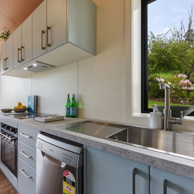 Kitchen with light cabinets, marble countertops, a window with a garden view, and bottles of sparkling water on the counter.
