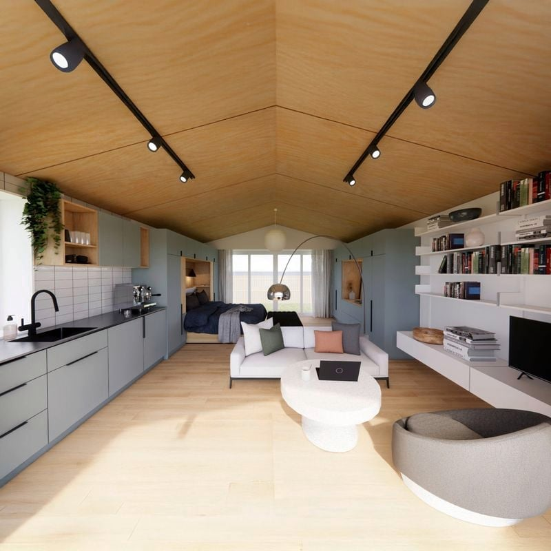 Open-concept living space featuring a kitchen, couch, and bed with wood-paneled ceiling, white shelves with books, and large windows