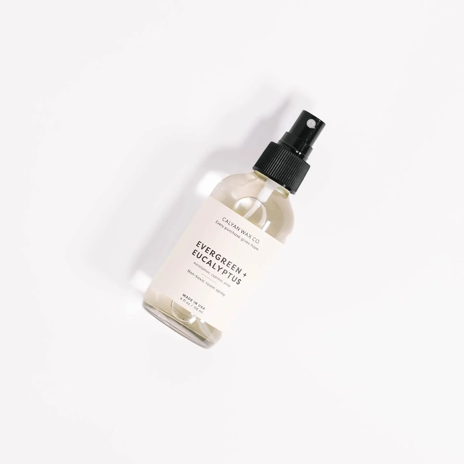 A clear spray bottle labeled 'Evergreen + Eucalyptus' by Calyan Wax Co., containing a room spray, placed on a white background.