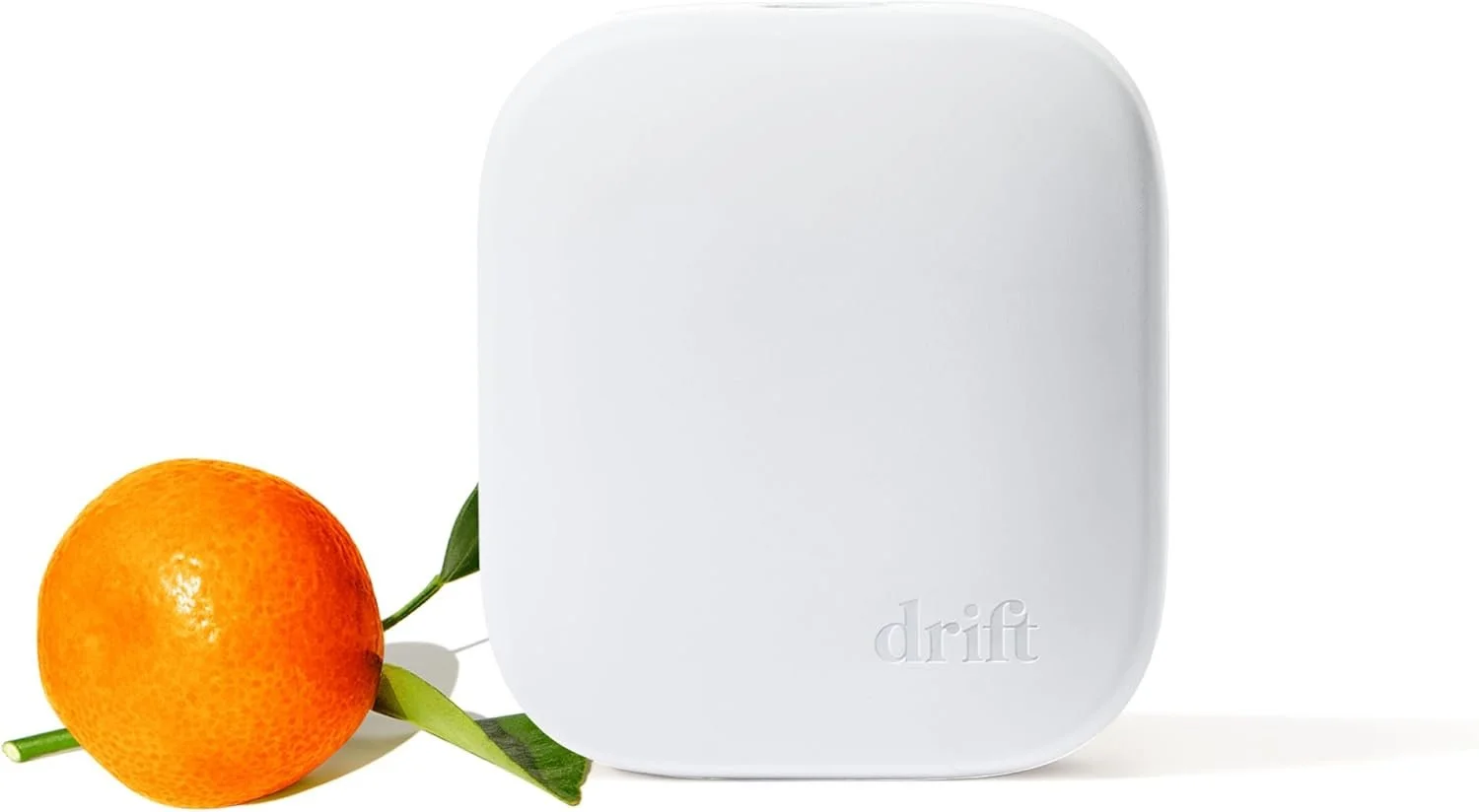 A white square device with rounded edges and the word "drift" embossed on it, placed next to an orange with green leaves.